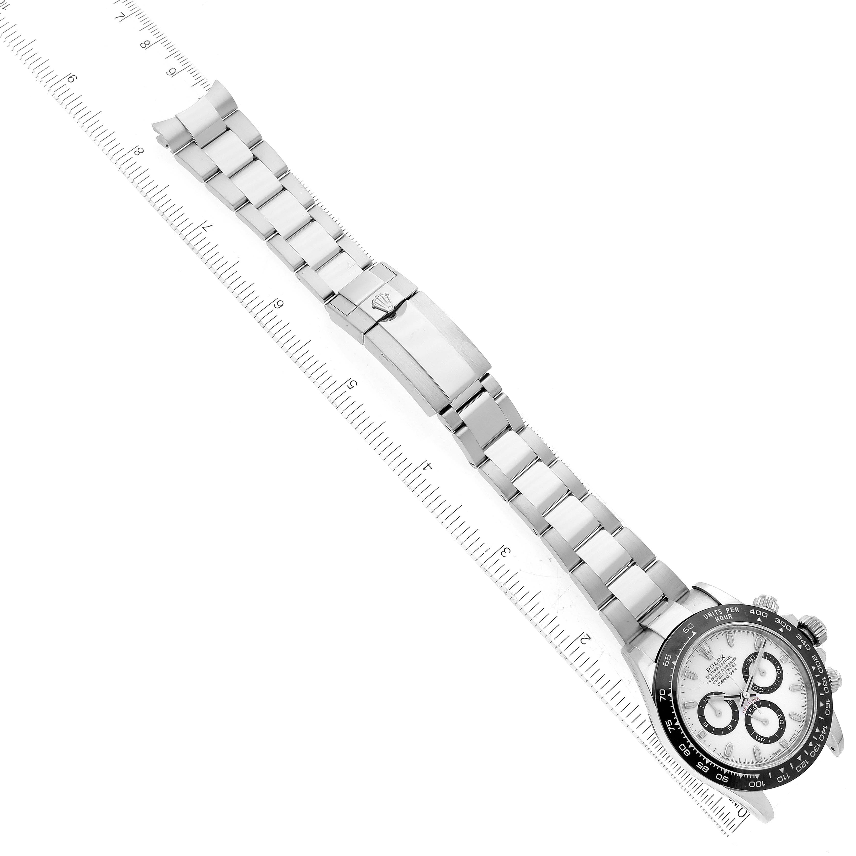 This image shows a top-down view of a Rolex Daytona 116500 Men's Stainless Steel White Dial 116500 Men's Stainless Steel White Dial watch featuring its strap, clasp, and face with a ruler for scale.