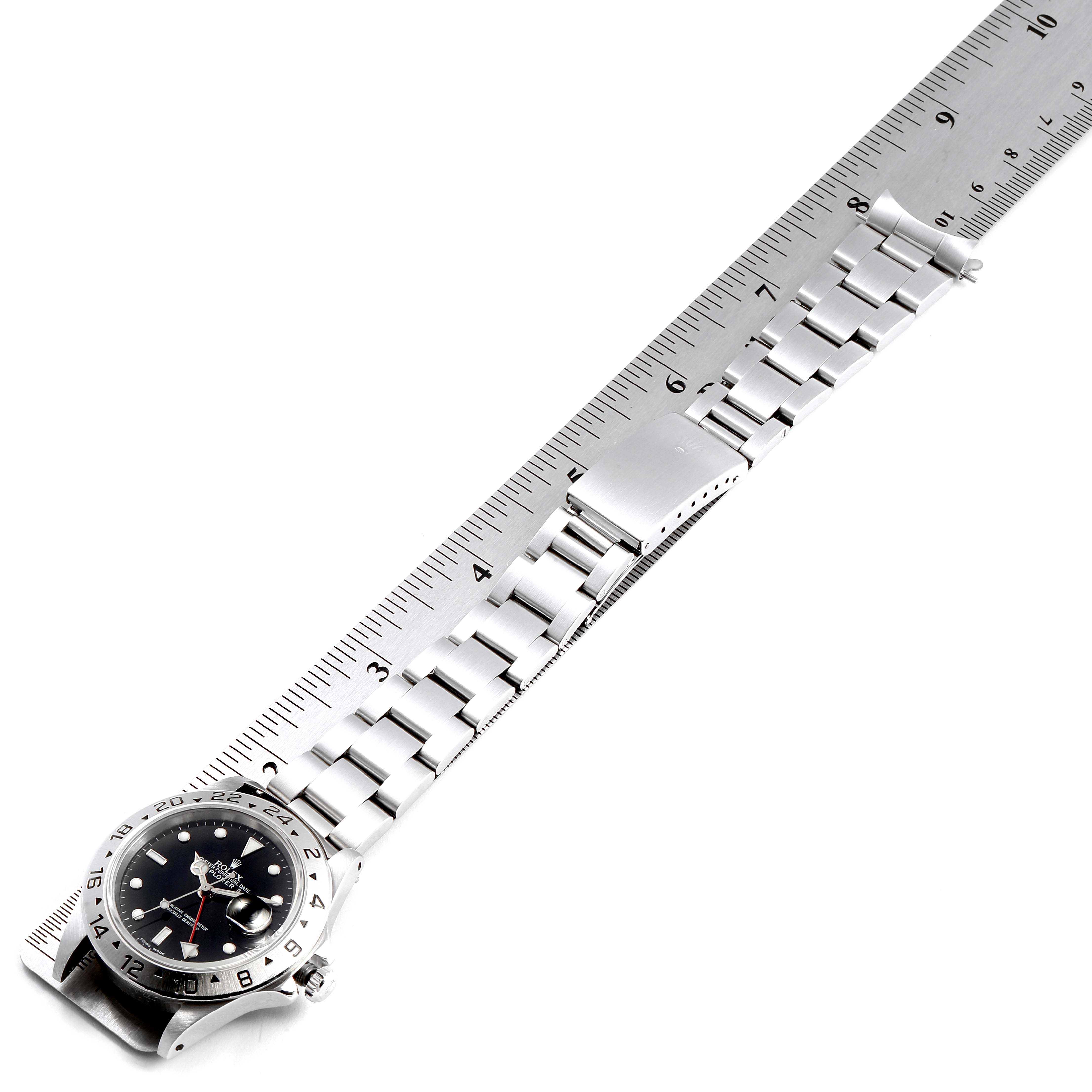 The image shows a Rolex Explorer 16570 Men
s Stainless Steel Black Dial 16570 Men
s Stainless Steel Black Dial watch laid flat next to a ruler, displaying the face, bezel, and metal band.