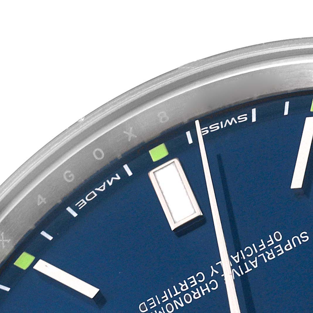 This close-up shows the dial of a Rolex Oyster Perpetual 114300 Men's Stainless Steel Blue Dial 114300 Men's Stainless Steel Blue Dial watch, specifically the hour markers and part of the text.