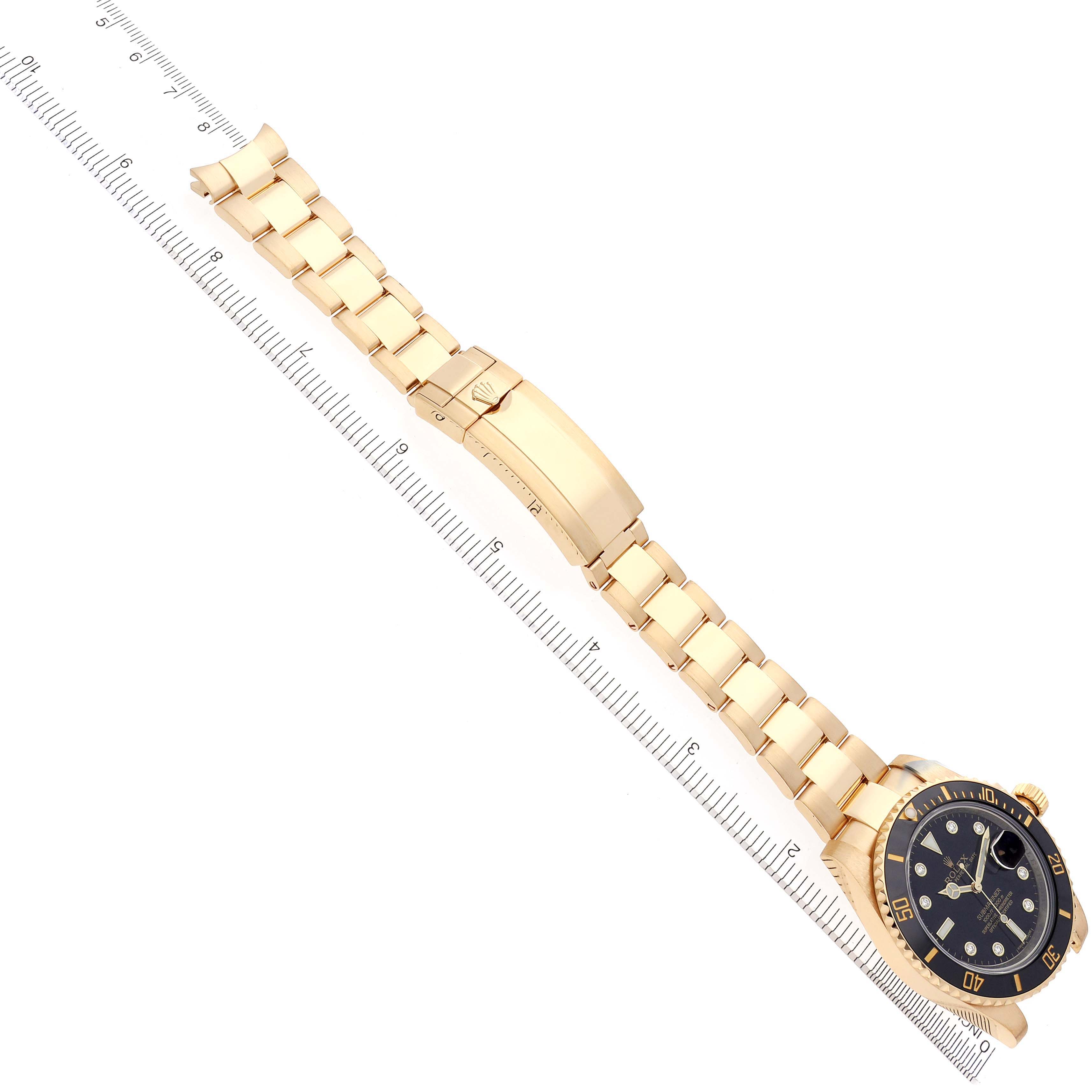 The Rolex Submariner 116618 Men's Yellow Gold Black Dial 116618 Men's Yellow Gold Black Dial watch is shown at a top-down angle, displaying the bracelet, clasp, and watch face alongside a ruler.