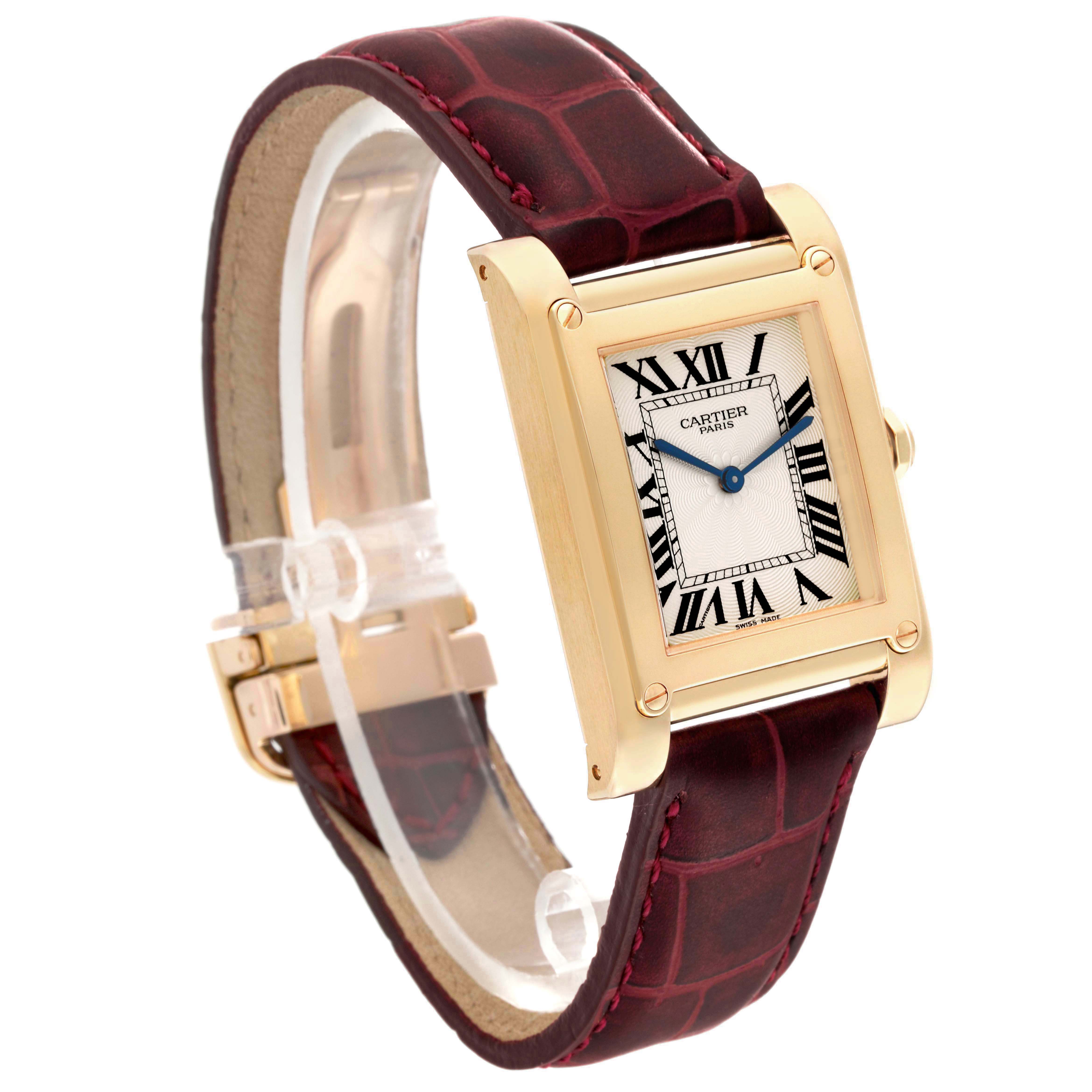 The Cartier Tank à Vis watch is shown at a slight angle, displaying its rectangular face, gold casing, and maroon strap.