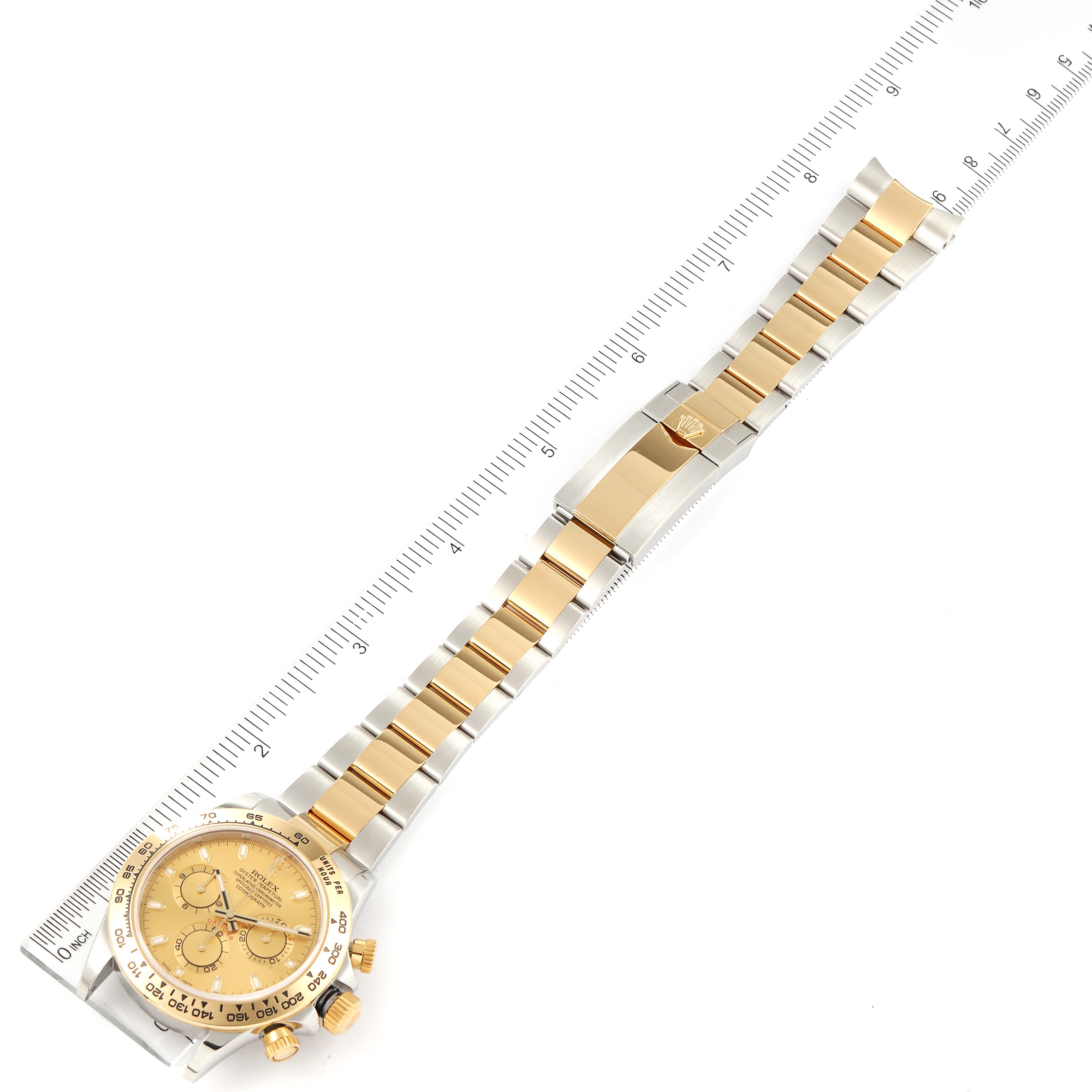 The Rolex Daytona 116503 Men's Steel and Gold (two tone) Champagne Dial 116503 Men's Steel and Gold (two tone) Champagne Dial watch is shown from a top-down angle, highlighting its dial, bracelet, and clasp next to a ruler for scale.