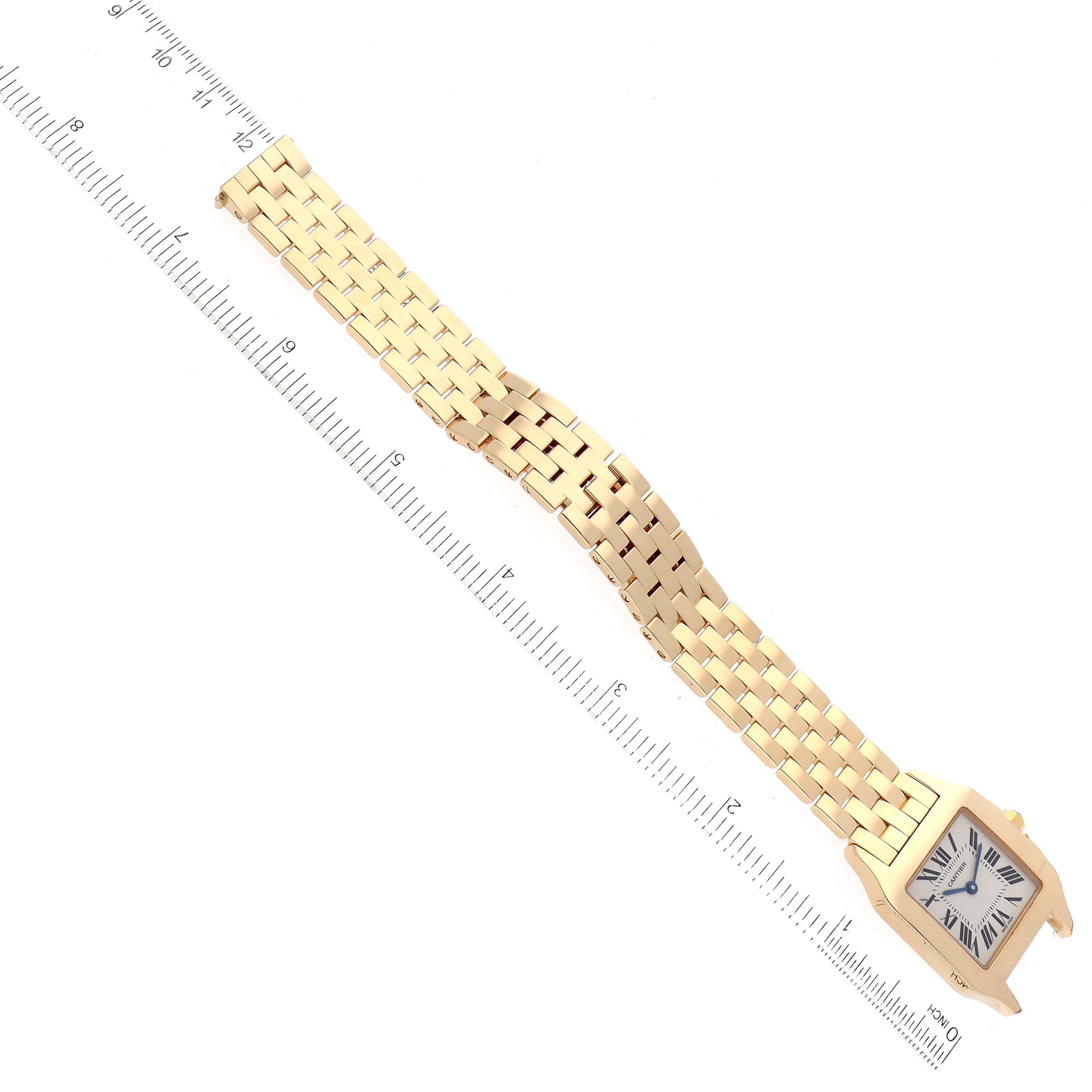 The image shows a Santos Demoiselle model by Cartier, displaying its gold case and bracelet, with a ruler for scale from a top-down angle.