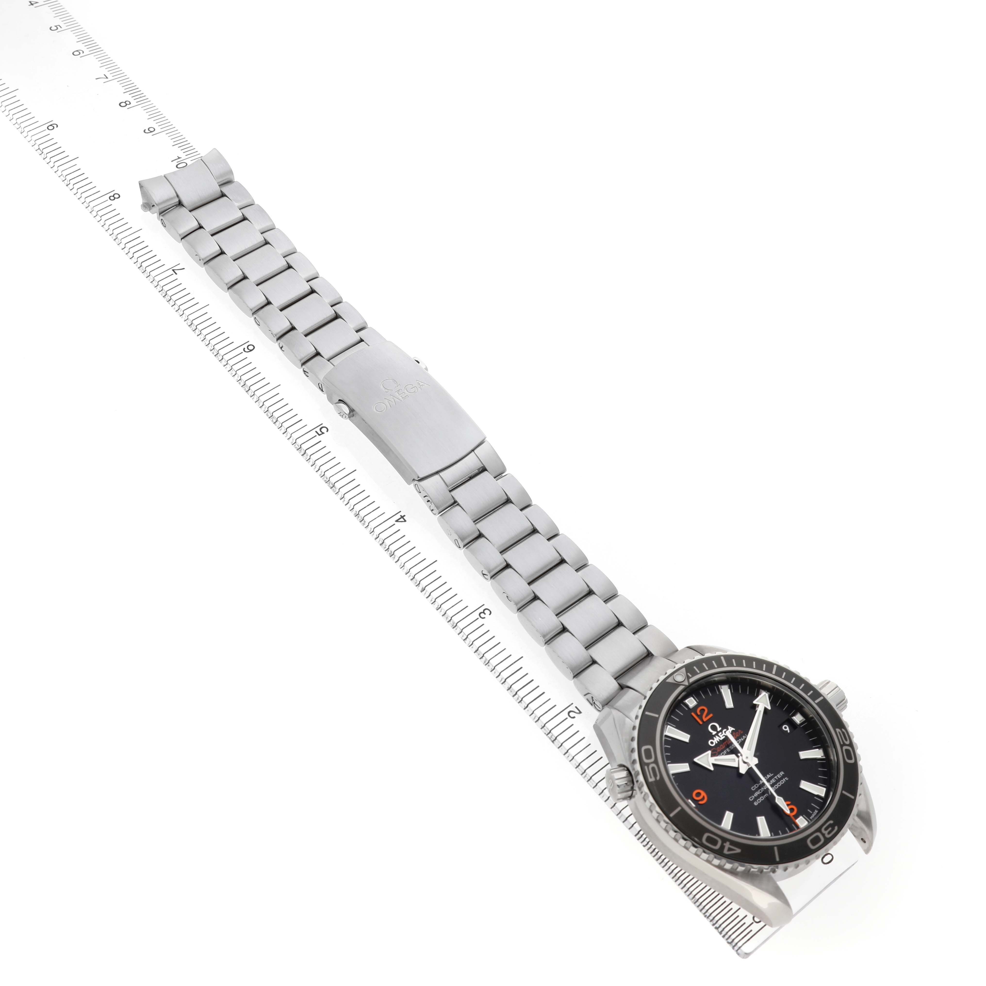 The image shows an Omega Planet Ocean 232.30.42.21.01.003 Men's Stainless Steel Black Dial watch at a diagonal angle, displaying the face, bezel, and full metal bracelet on a ruler.