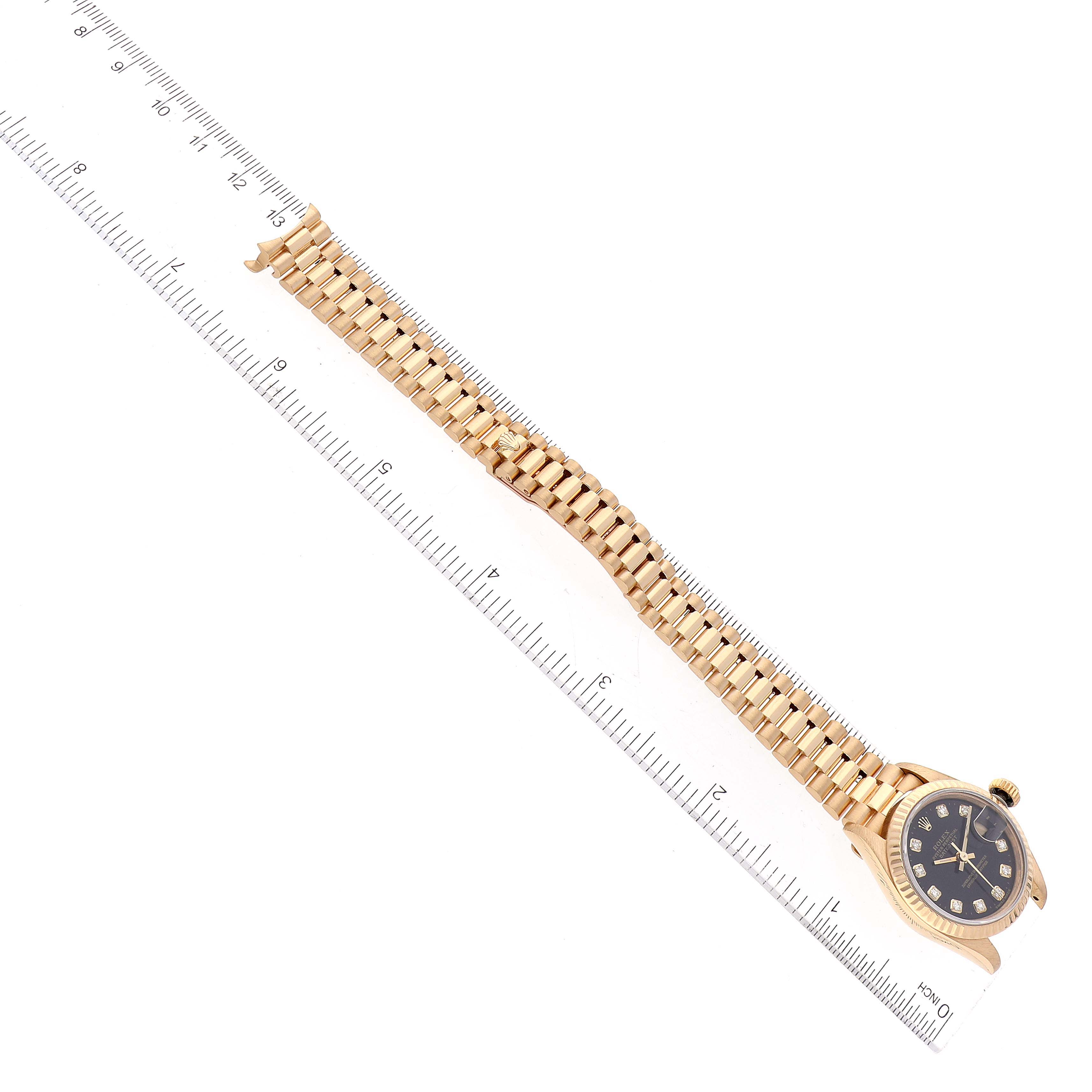 The image shows a Rolex President 69178 Women's Yellow Gold Black Dial 69178 Women's Yellow Gold Black Dial model watch laid flat next to a ruler, displaying the band and the face with its bezels.