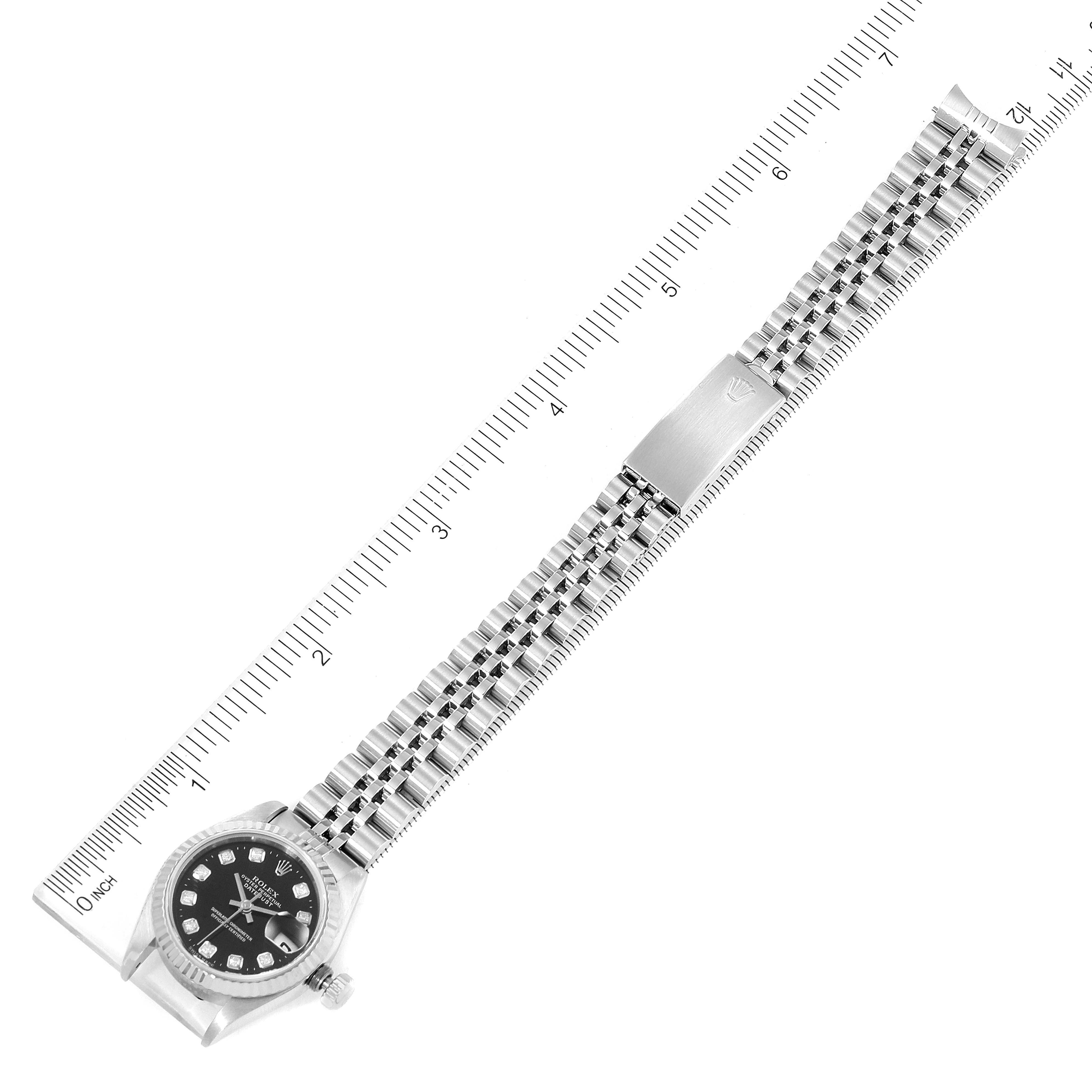 The image shows a top-down view of a Rolex Datejust 69174 Women's Stainless Steel Black Dial 69174 Women's Stainless Steel Black Dial watch with a full bracelet and a measuring ruler beside it.