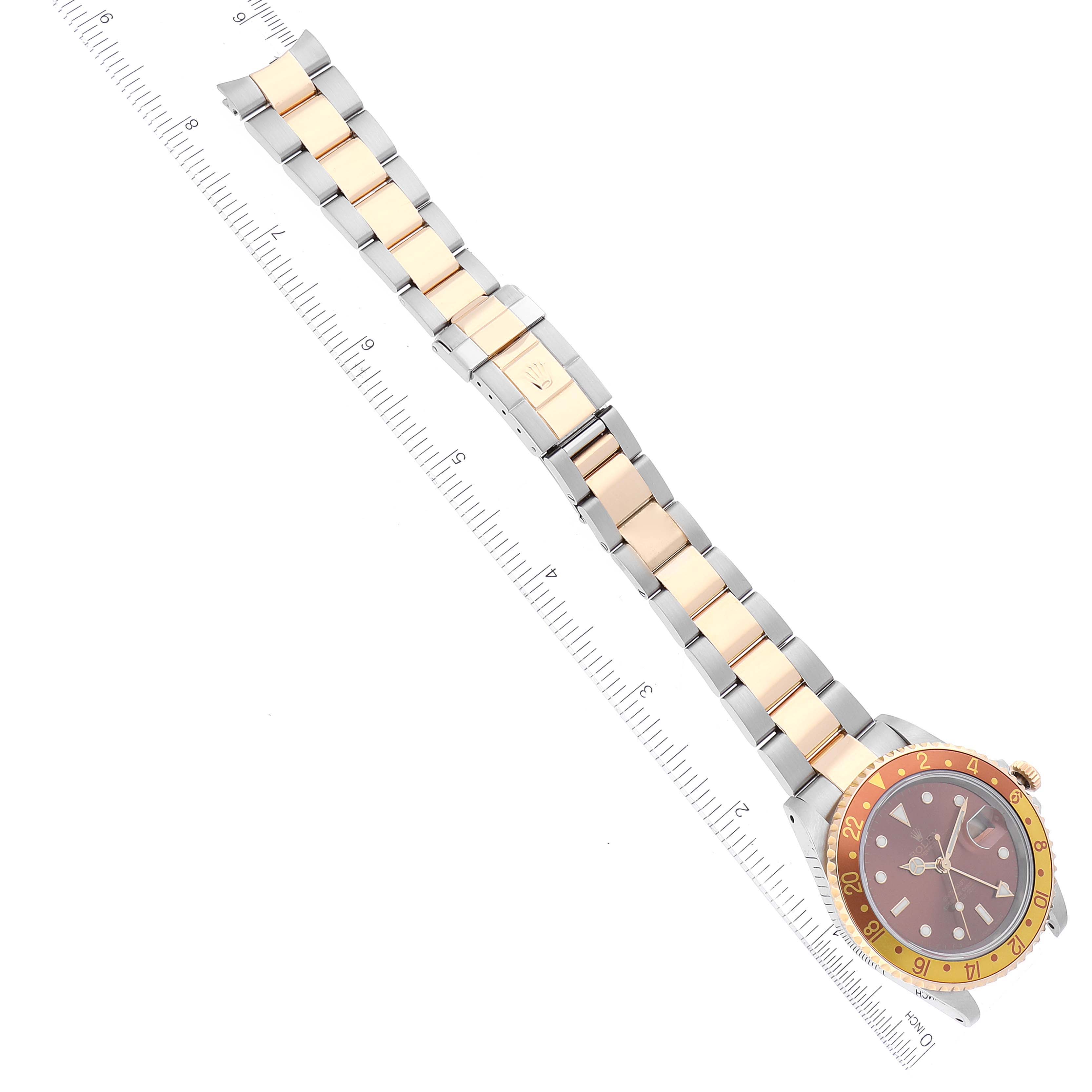 The image shows the face, bezel, and entire band of a Rolex GMT-Master 16713 Men's Steel and Gold (two tone) Brown Dial 16713 Men's Steel and Gold (two tone) Brown Dial watch, positioned diagonally with a ruler beside it.