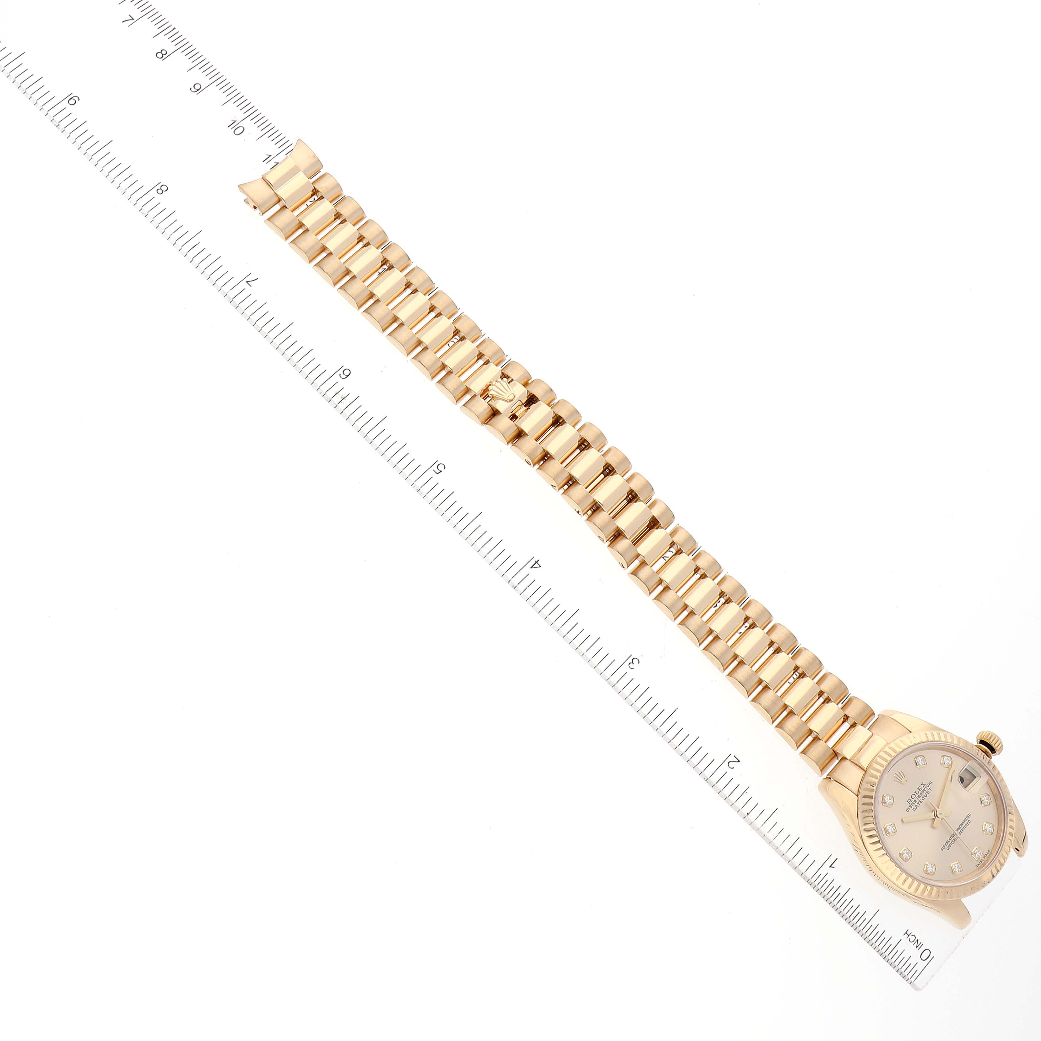 The image shows the President model of a Rolex watch laid flat with a ruler alongside, displaying the entire watch band and face.