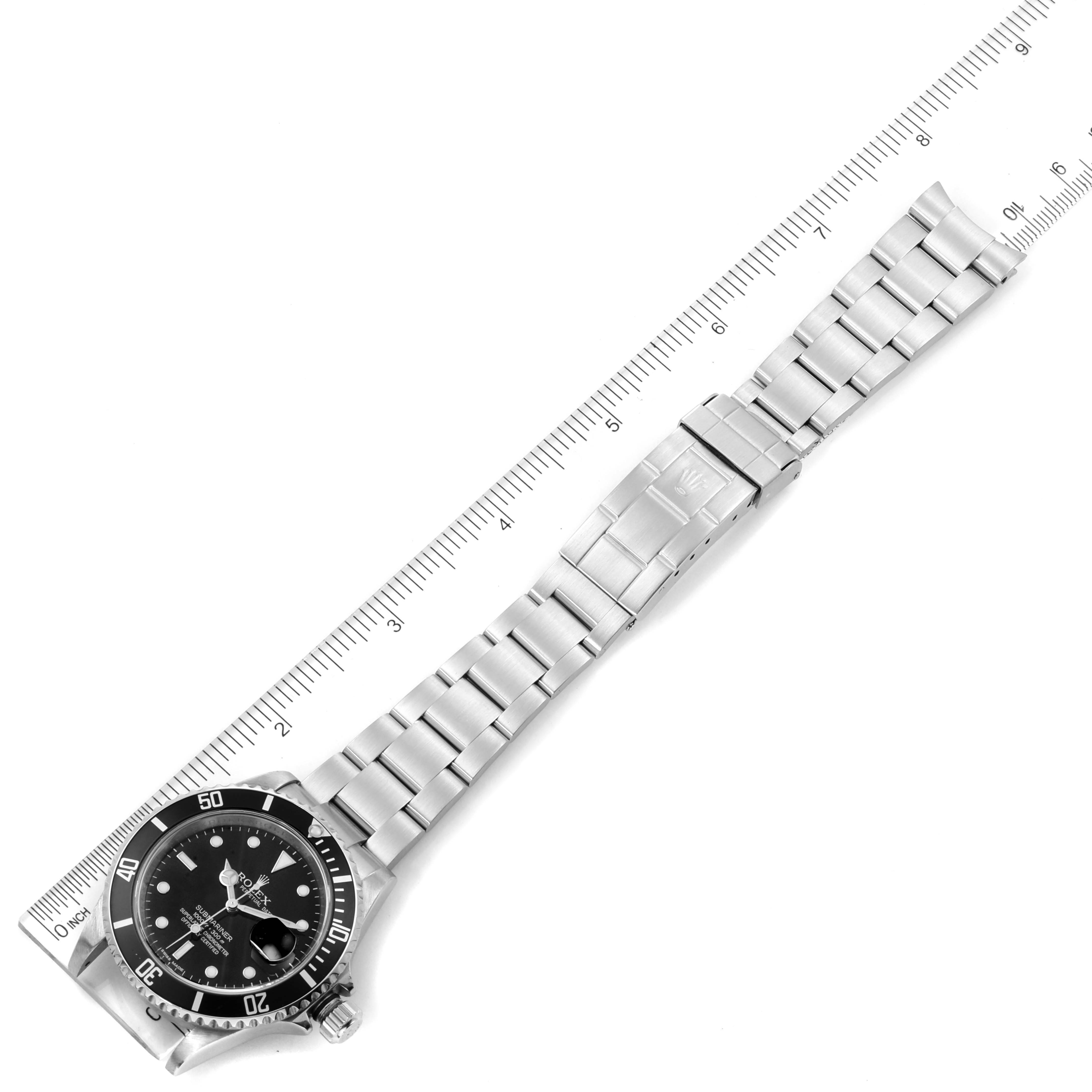 This image shows a top-down view of a Rolex Submariner 16610 Men
s Stainless Steel Black Dial 16610 Men
s Stainless Steel Black Dial watch with its bezel, dial, bracelet, and clasp alongside a ruler.