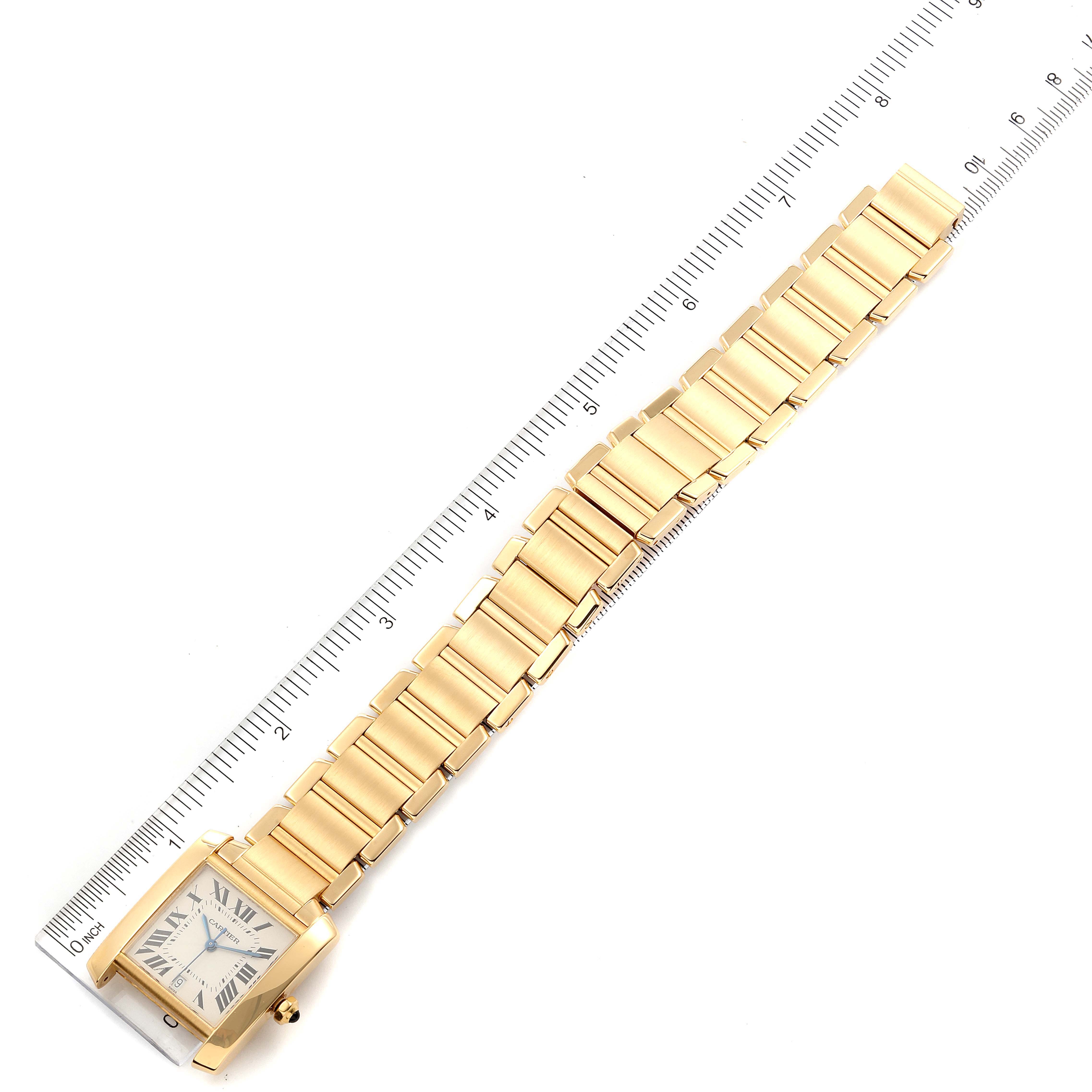 The Cartier Tank Française watch is shown laid flat, displaying its face and gold bracelet, next to a ruler for scale.