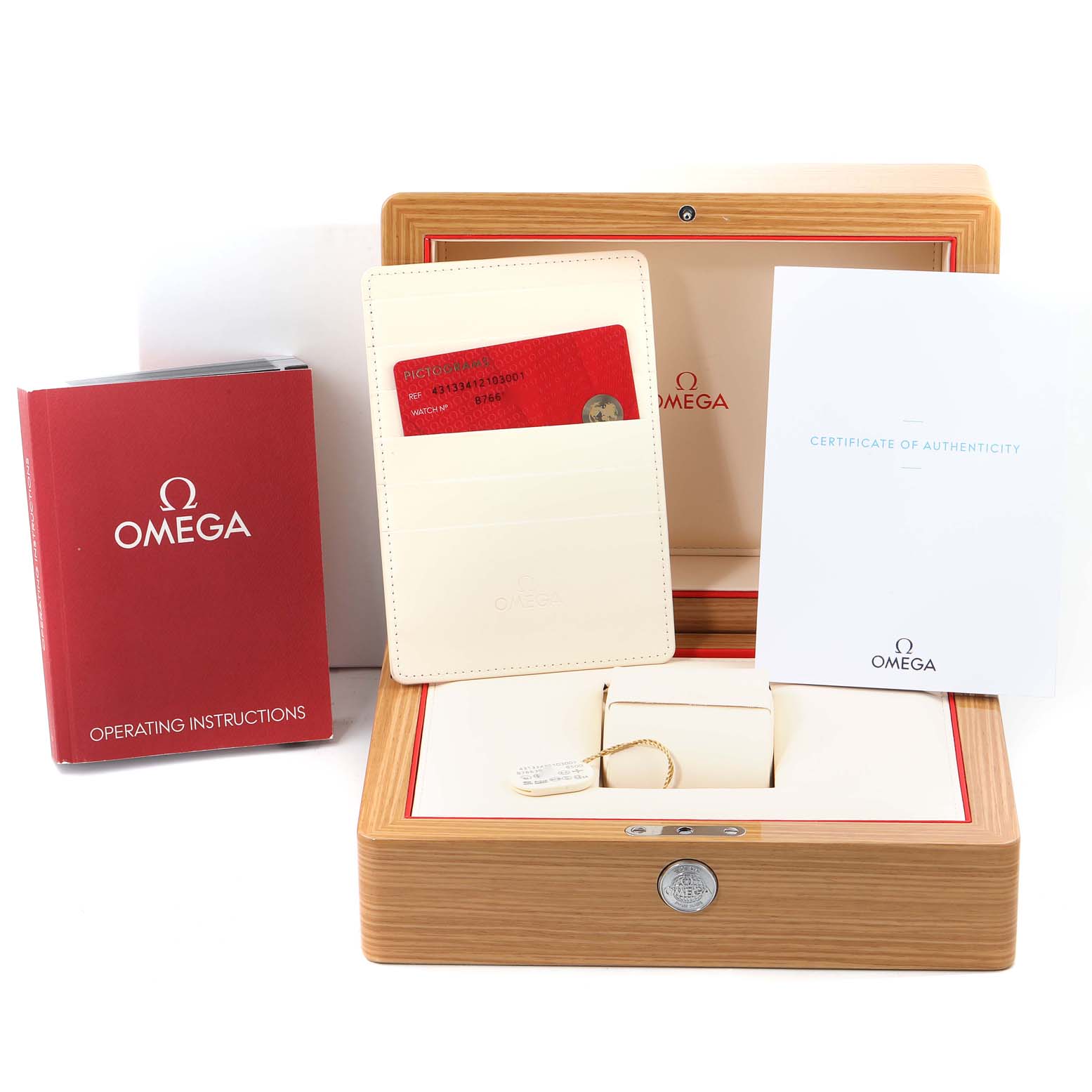 The image shows accessories for Omega's De Ville model: a red operating instructions book, a cardholder with a red card, and a certificate of authenticity, all placed on an open wooden watch box.