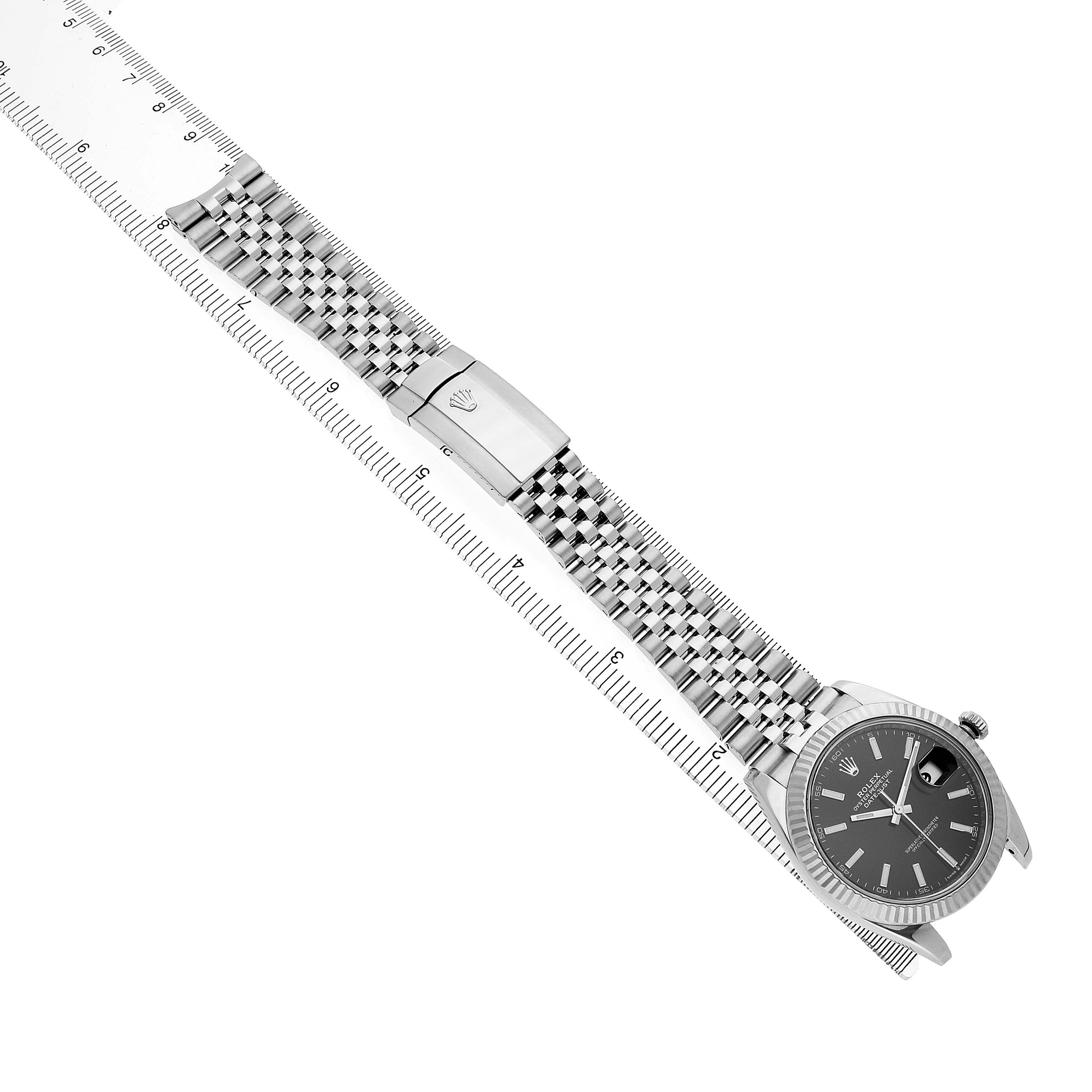 The Rolex Datejust 41 M126334-0018 Men's Stainless Steel Black Dial is shown at a diagonal angle, displaying the watch face and full bracelet laid atop a ruler.