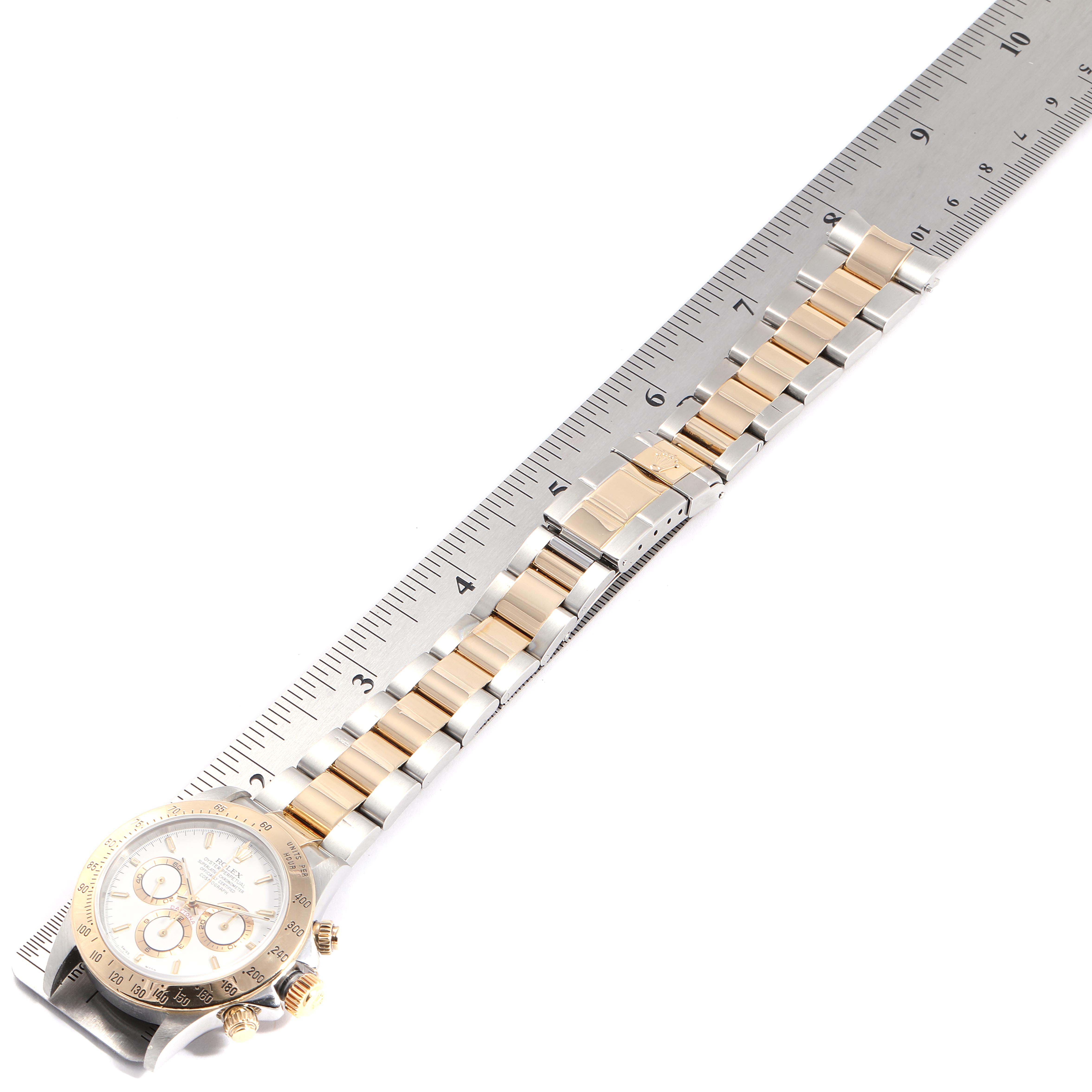 The image shows a Rolex Daytona 116523 Men
s Steel and Gold (two tone) White Dial 116523 Men
s Steel and Gold (two tone) White Dial watch laid flat alongside a ruler, displaying the band and partial face of the watch.