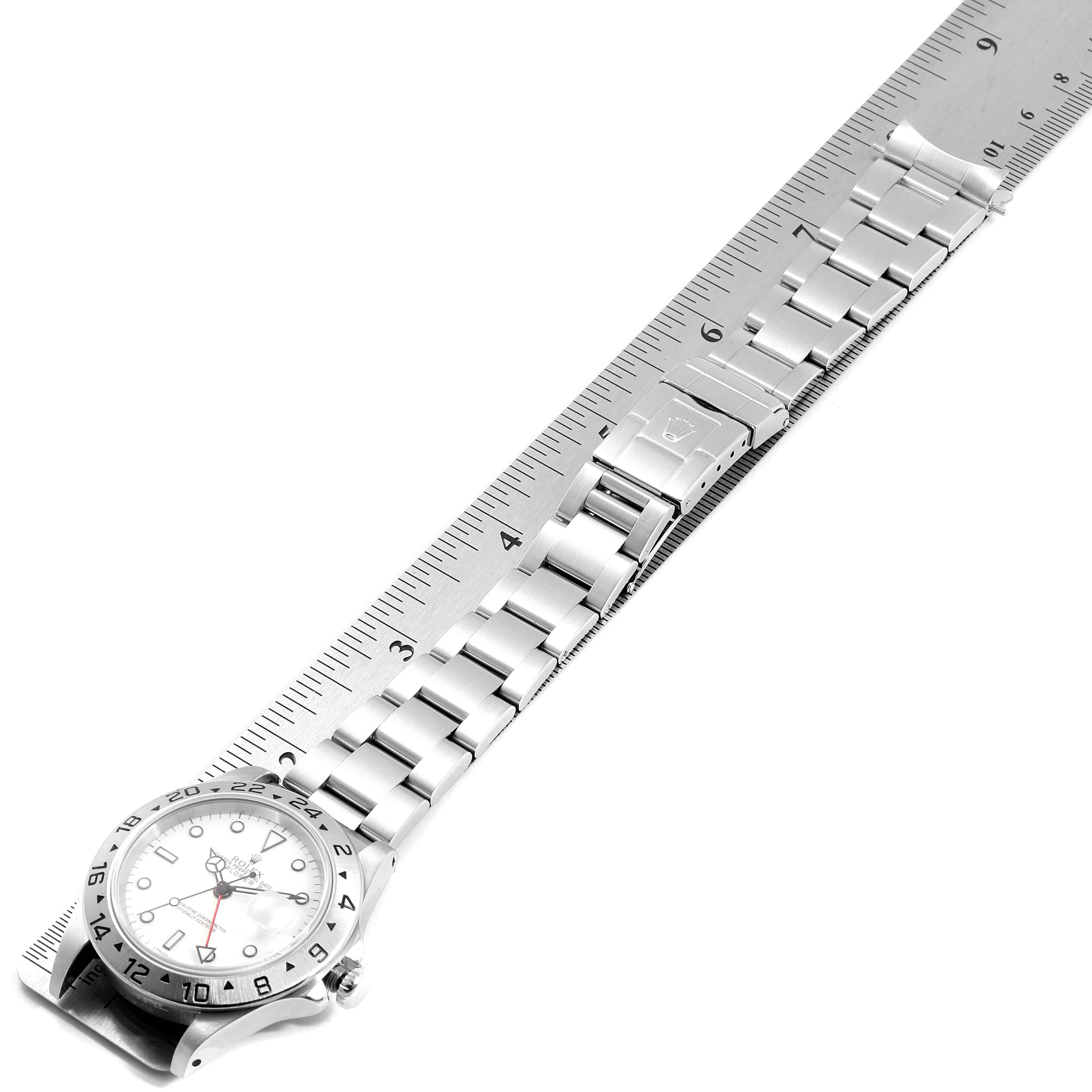The Rolex Explorer 16570 Men
s Stainless Steel White Dial 16570 Men
s Stainless Steel White Dial watch is shown laid flat, displaying its face, bezel, bracelet, and clasp alongside a ruler.