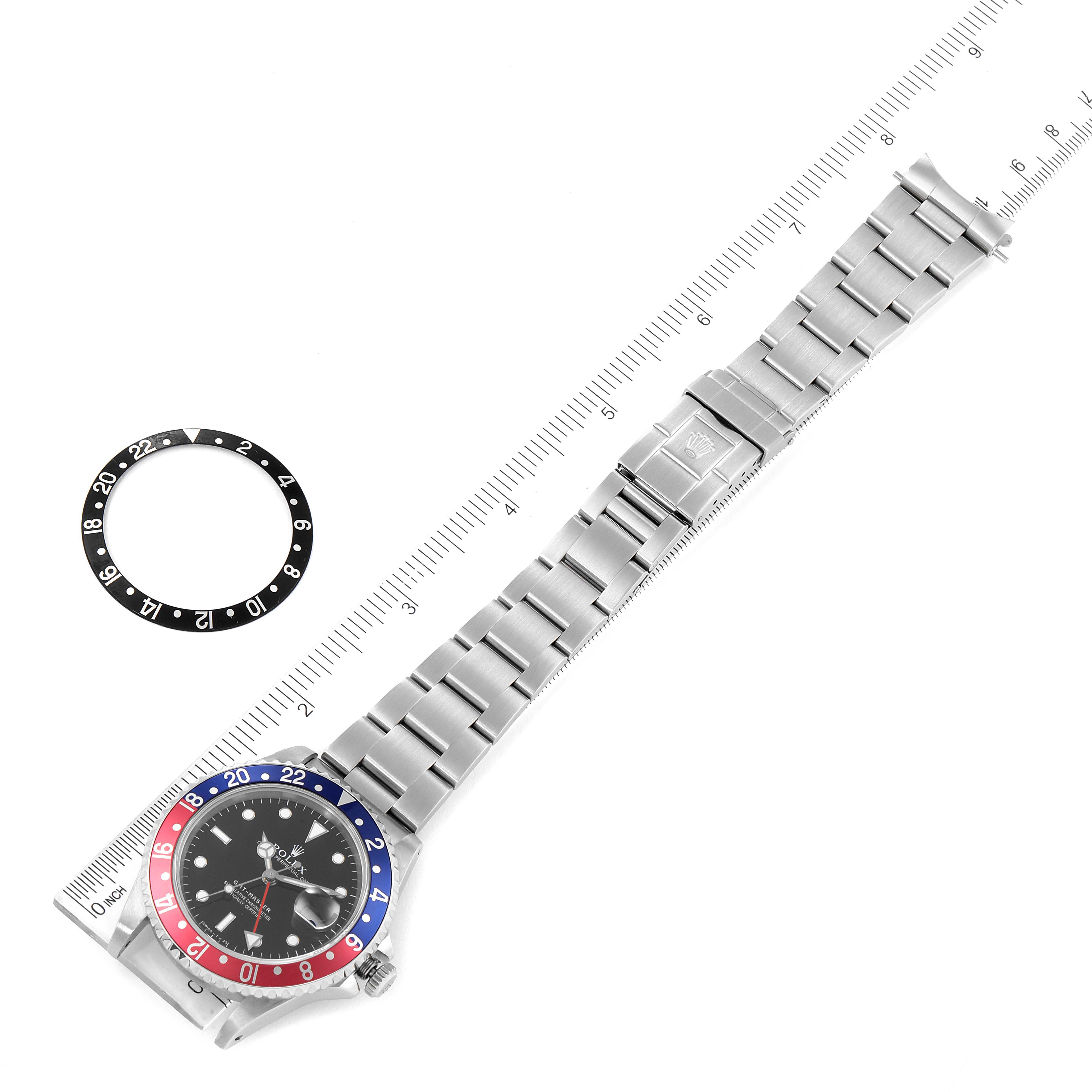 The image shows a top view of the Rolex GMT-Master 16700 Men
s Stainless Steel Black Dial 16700 Men
s Stainless Steel Black Dial watch alongside an extra bezel insert and a measuring ruler.