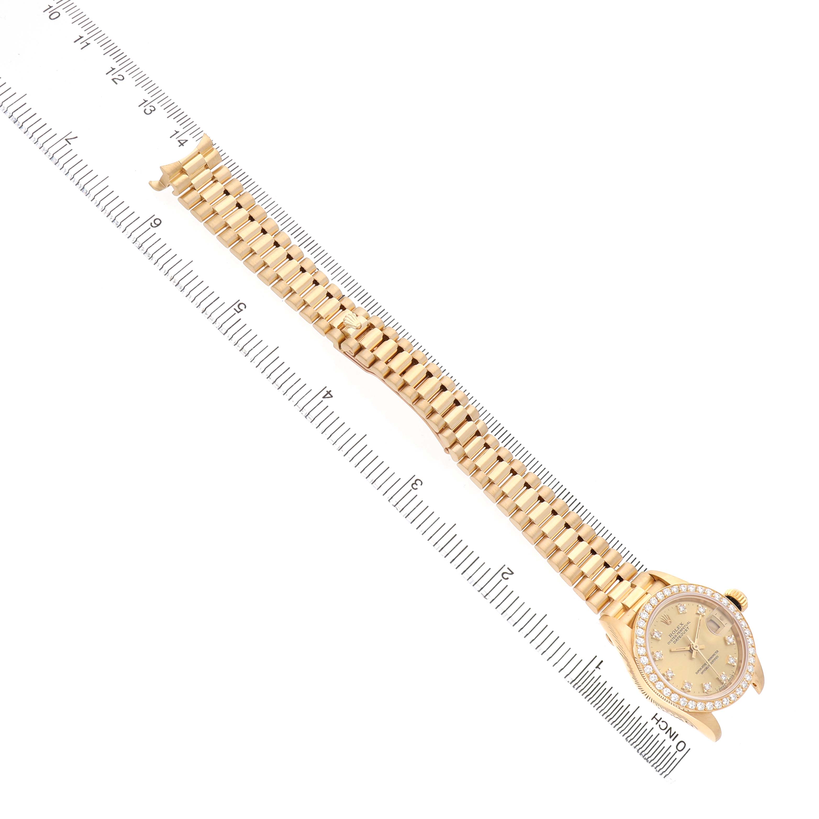The Rolex President 79138 Women's Yellow Gold Champagne Dial watch is shown at a top-down angle, displaying its full band and face with diamonds, next to a measuring ruler.