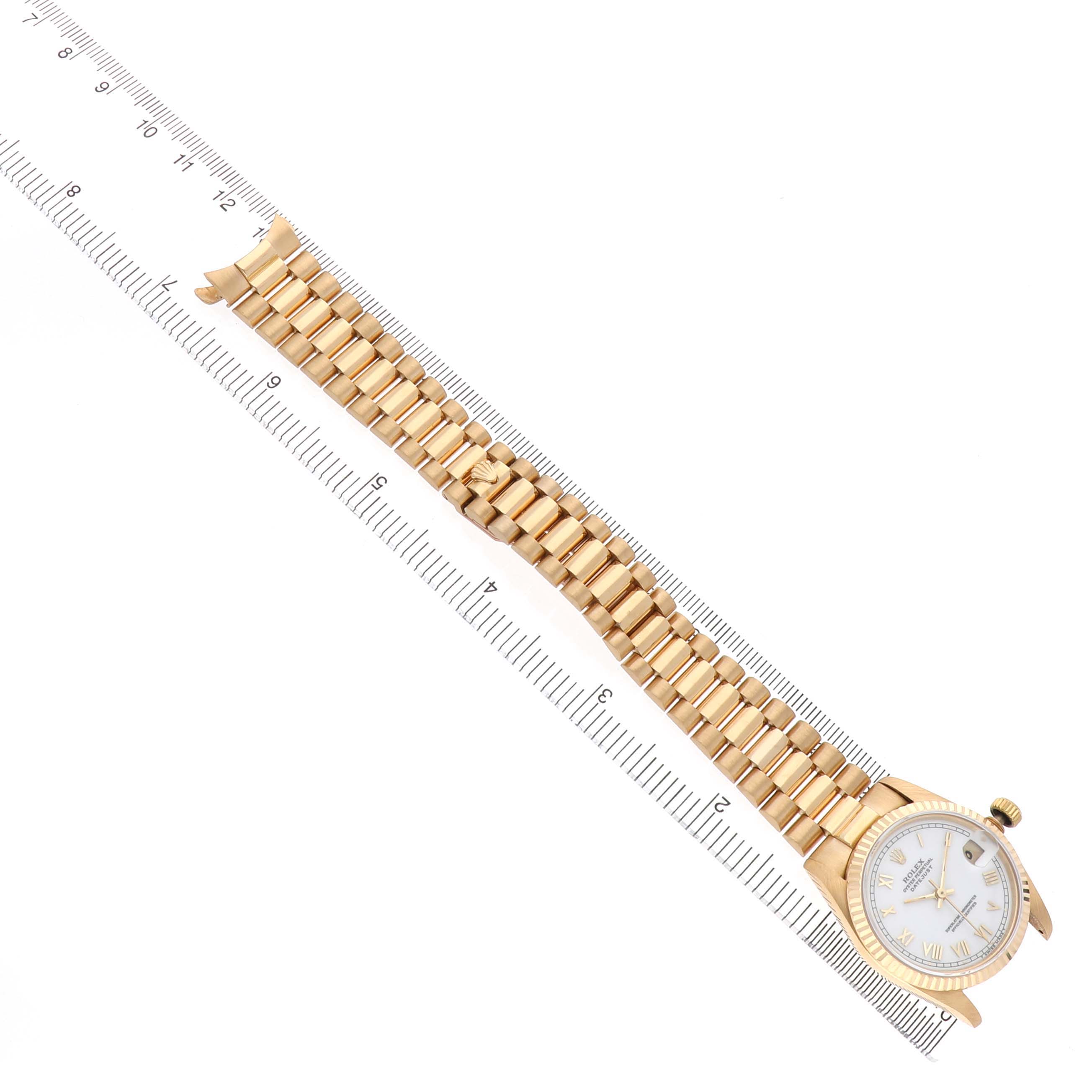The Rolex Datejust 68278 Women's Yellow Gold White Dial watch is displayed from an overhead angle, showing the full bracelet and watch face alongside a ruler for scale.