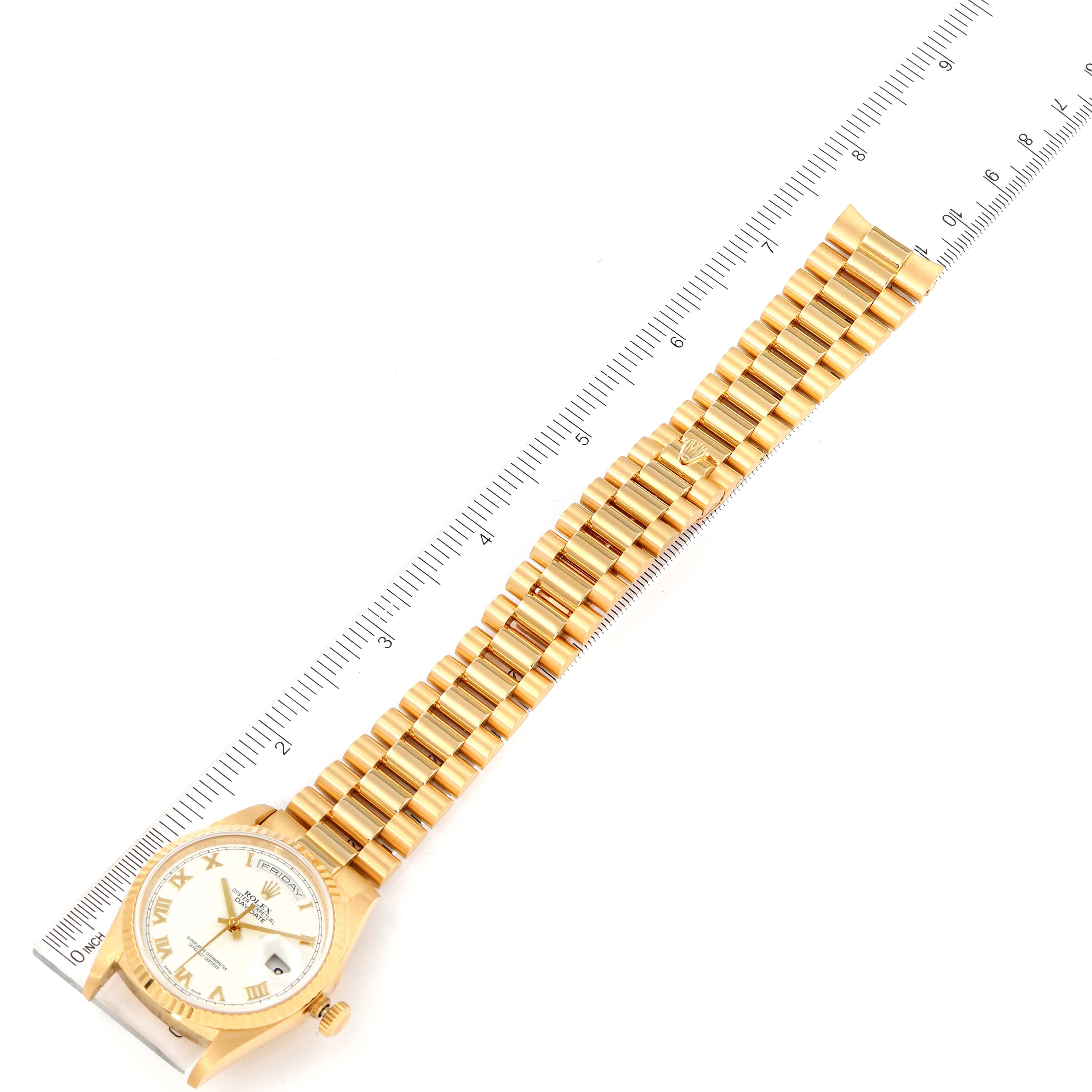 The image shows a Rolex President 18238 Men
s Yellow Gold White Dial 18238 Men
s Yellow Gold White Dial watch laid flat with a full view of the gold bracelet and dial next to a ruler. 