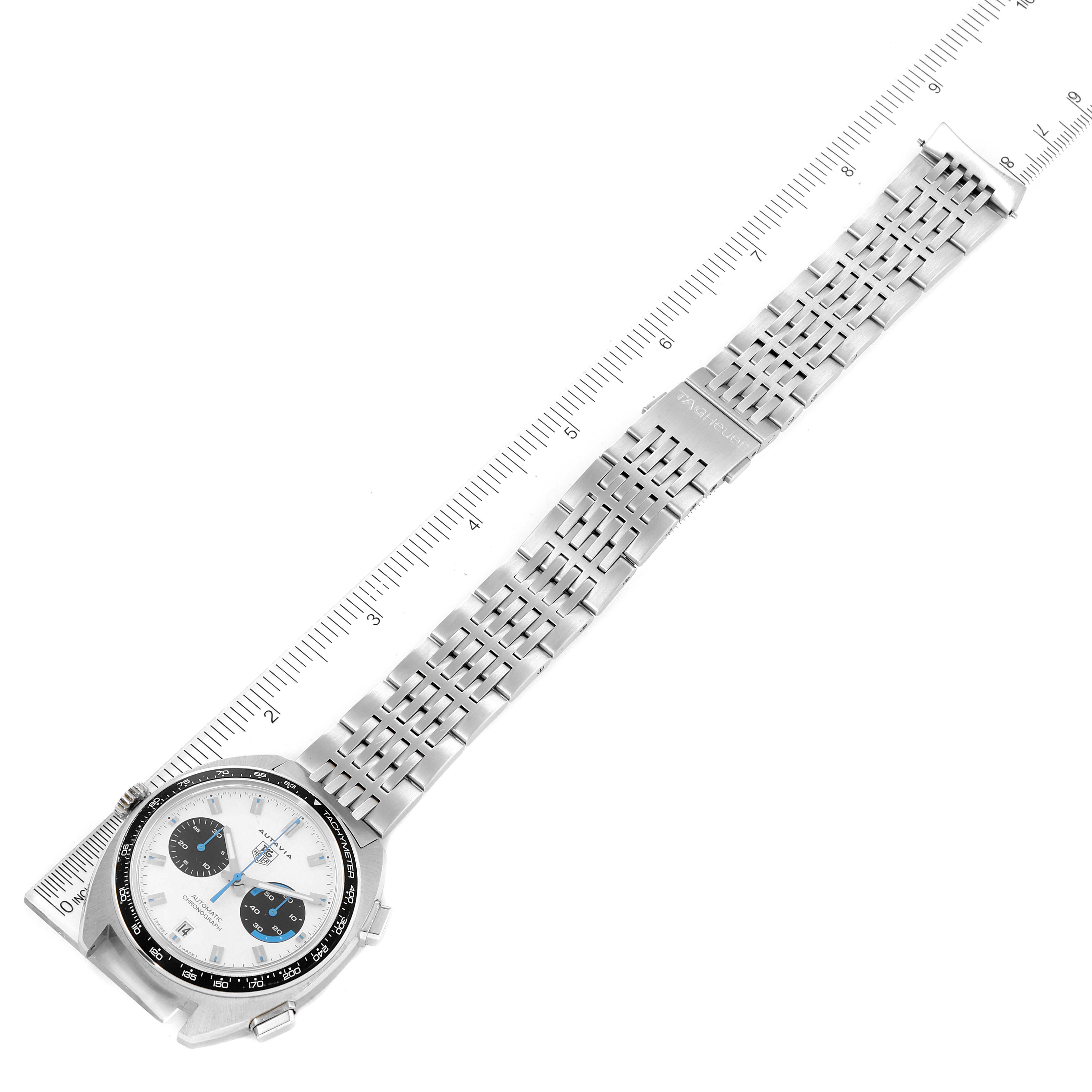 The image shows an overhead view of a Tag Heuer Autavia CY2110 Men's Stainless Steel White Dial CY2110 Men's Stainless Steel White Dial watch, showcasing its dial and metal bracelet alongside a measuring scale.