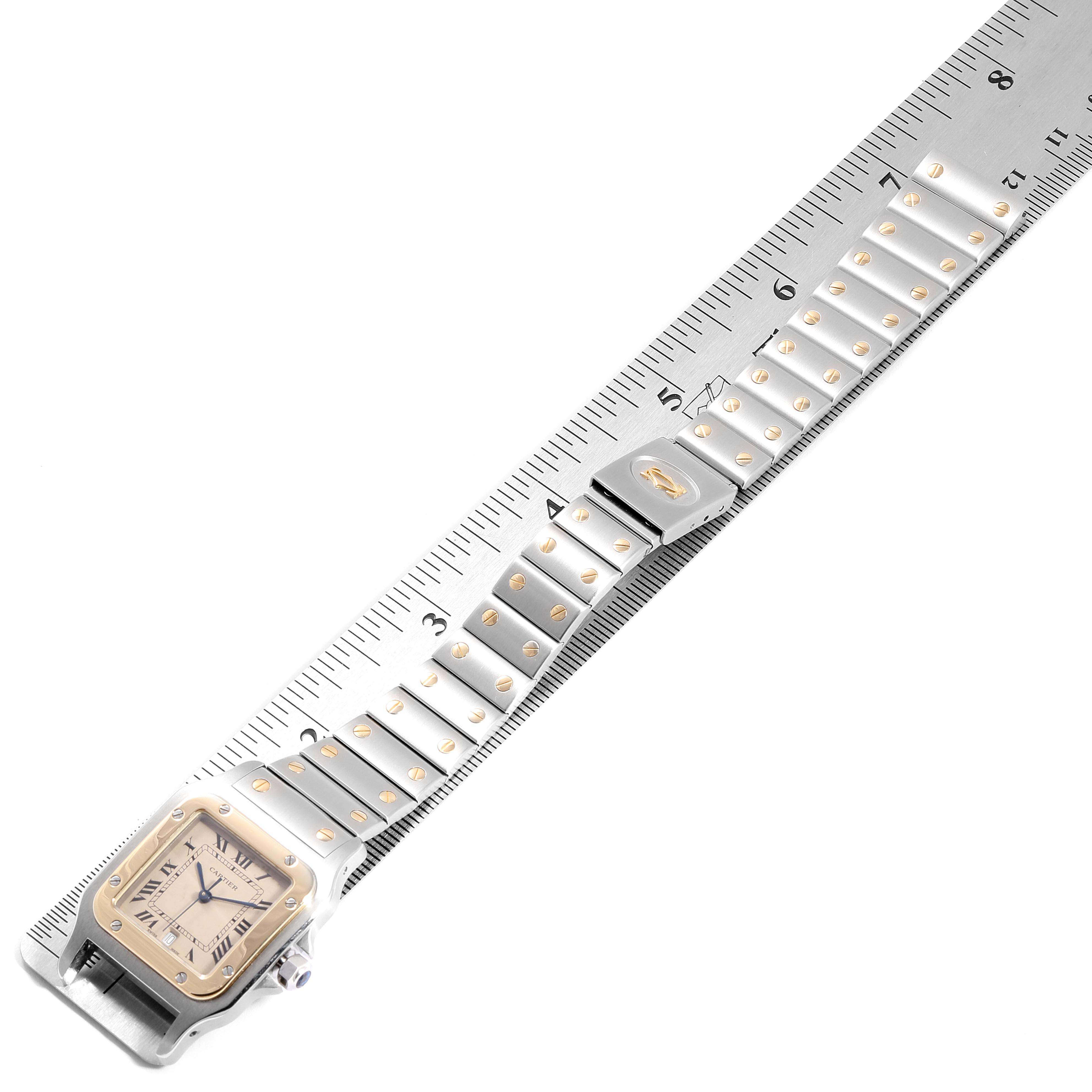 The Santos by Cartier watch is shown placed diagonally on a ruler, highlighting its face and bracelet.