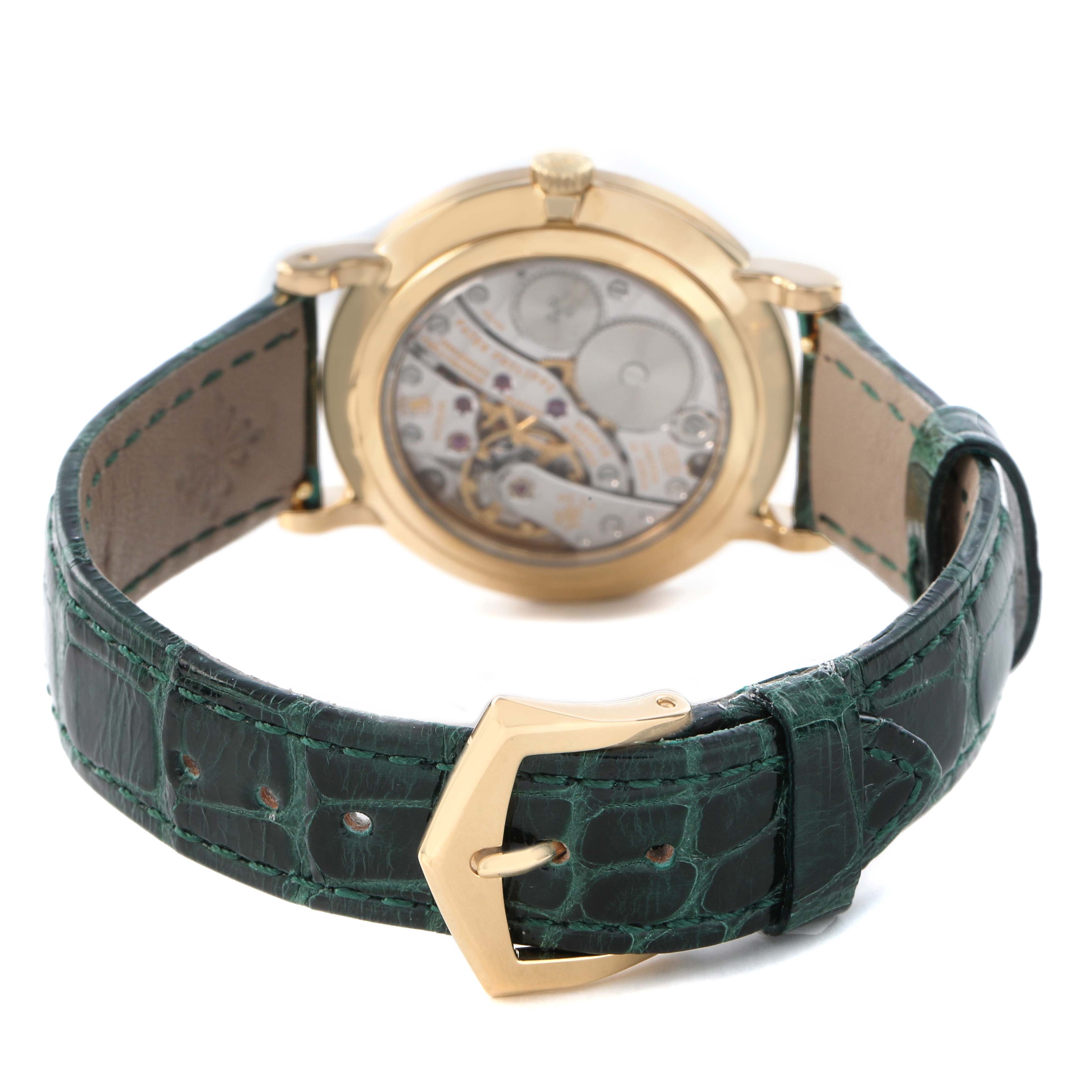 The image shows the back view of a Patek Philippe Calatrava 7119 / 7119J Women's Yellow Gold White Dial watch, highlighting the movement and green leather strap with a gold buckle.