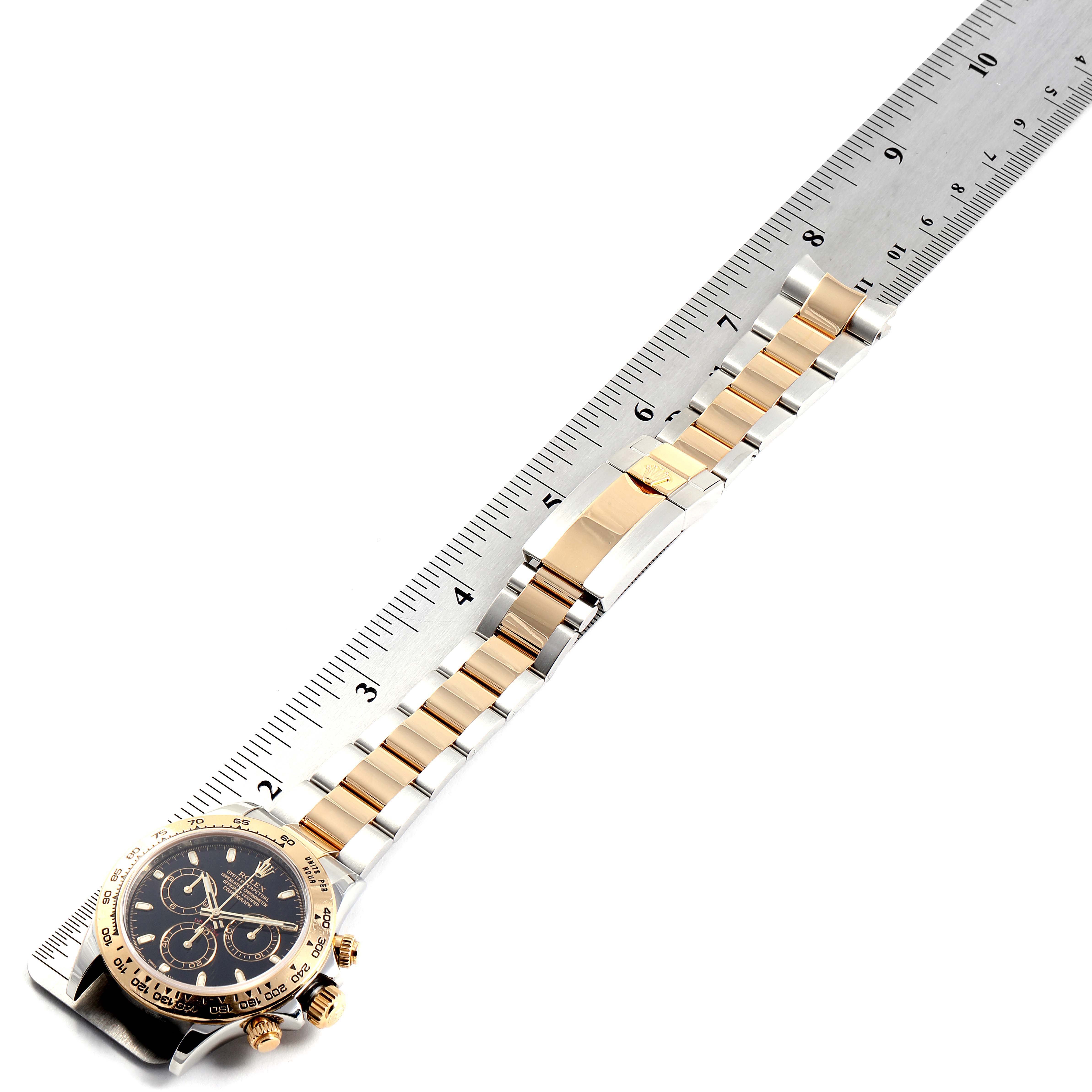 The Rolex Daytona 116503 Men's Steel and Gold (two tone) Black Dial 116503 Men's Steel and Gold (two tone) Black Dial watch is shown from a top view, highlighting its face, bezel, and bracelet next to a ruler.