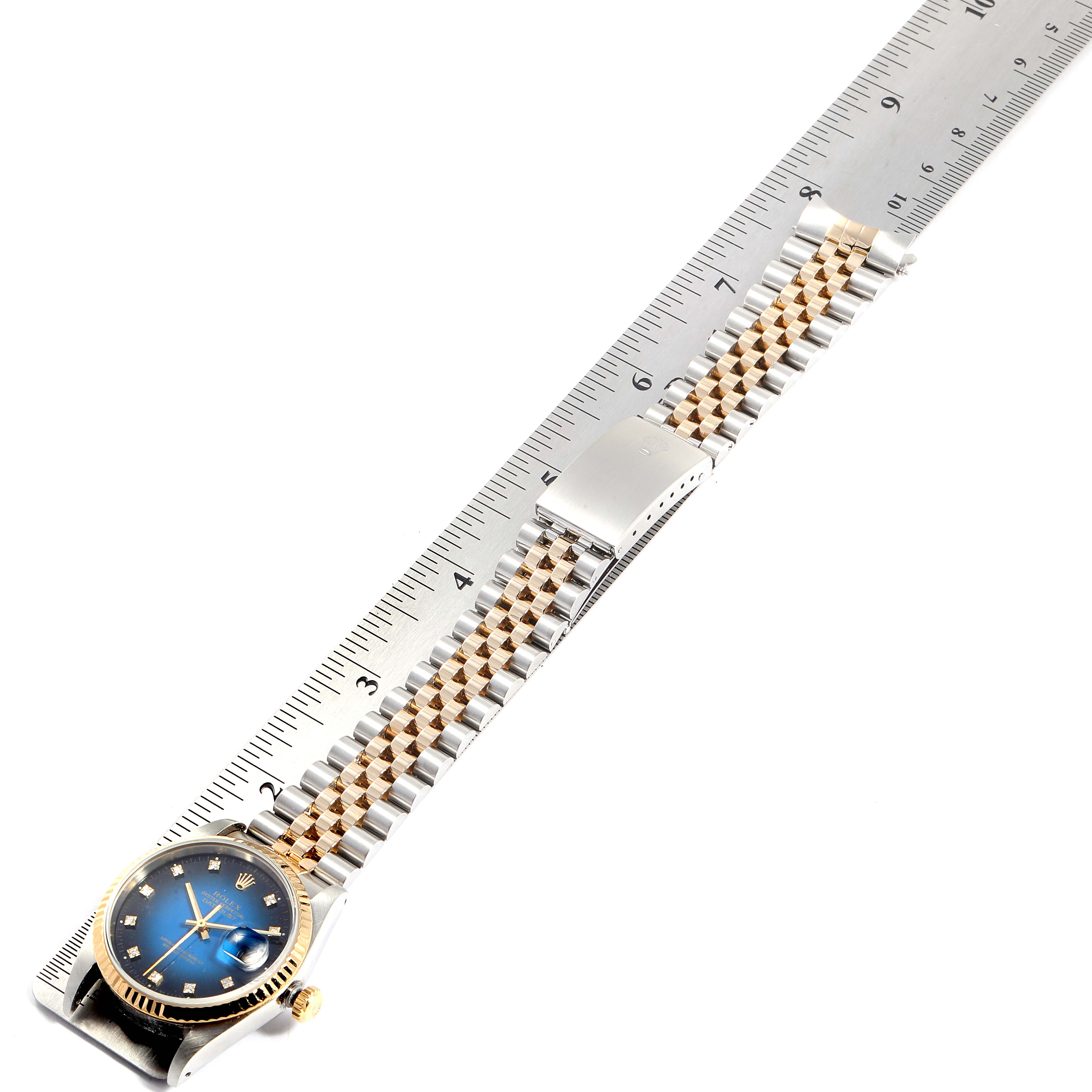 The image shows a Rolex Datejust 16233 Men
s Steel and Gold (two tone) Blue Dial 16233 Men
s Steel and Gold (two tone) Blue Dial watch positioned flat on a ruler, displaying its face, bracelet, and clasp.