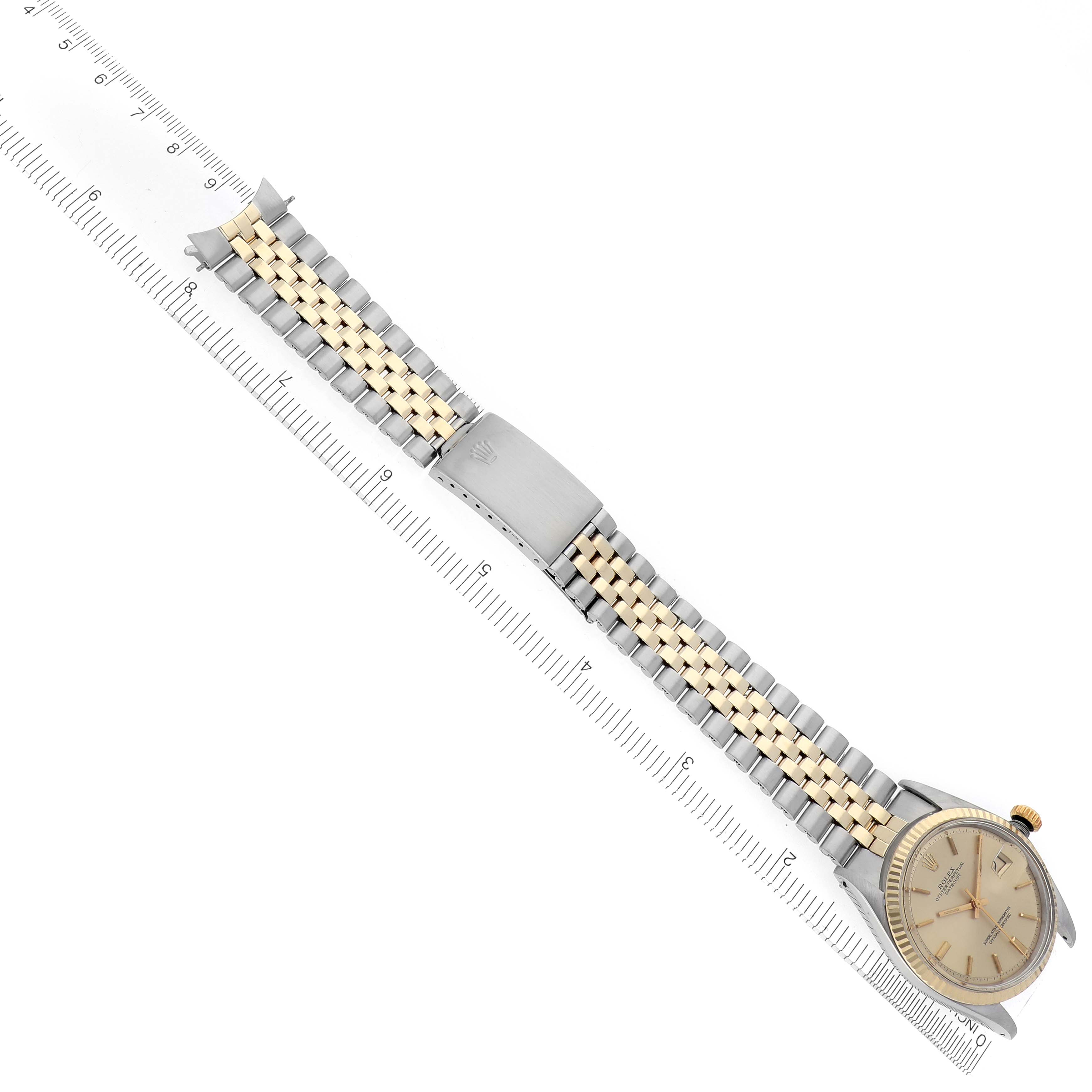 The Rolex Datejust 1601 Men's Steel and Gold (two tone) Champagne Dial 1601 Men's Steel and Gold (two tone) Champagne Dial watch is shown from a top-down angle, highlighting the two-tone bracelet and clasp alongside a ruler.