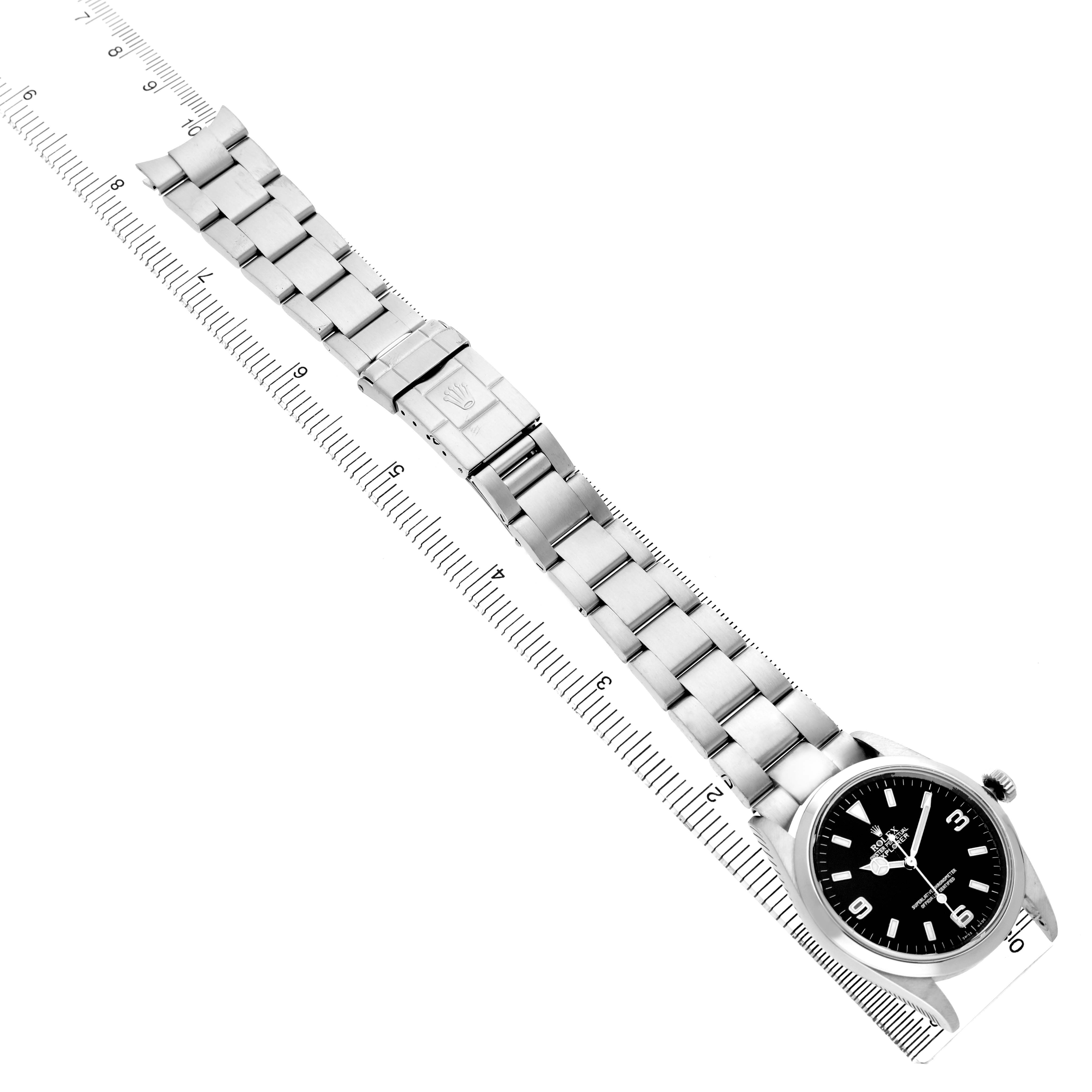The image shows a top view of a Rolex Explorer 114270 Men's Stainless Steel Black Dial watch, showcasing its full bracelet and case alongside a ruler for scale.