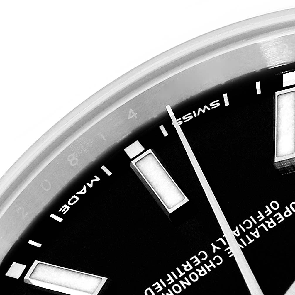 The image shows a close-up of the dial and hour markers of a Rolex Oyster Perpetual 114300 Men
s Stainless Steel Black Dial 114300 Men
s Stainless Steel Black Dial watch, viewed from an oblique angle.