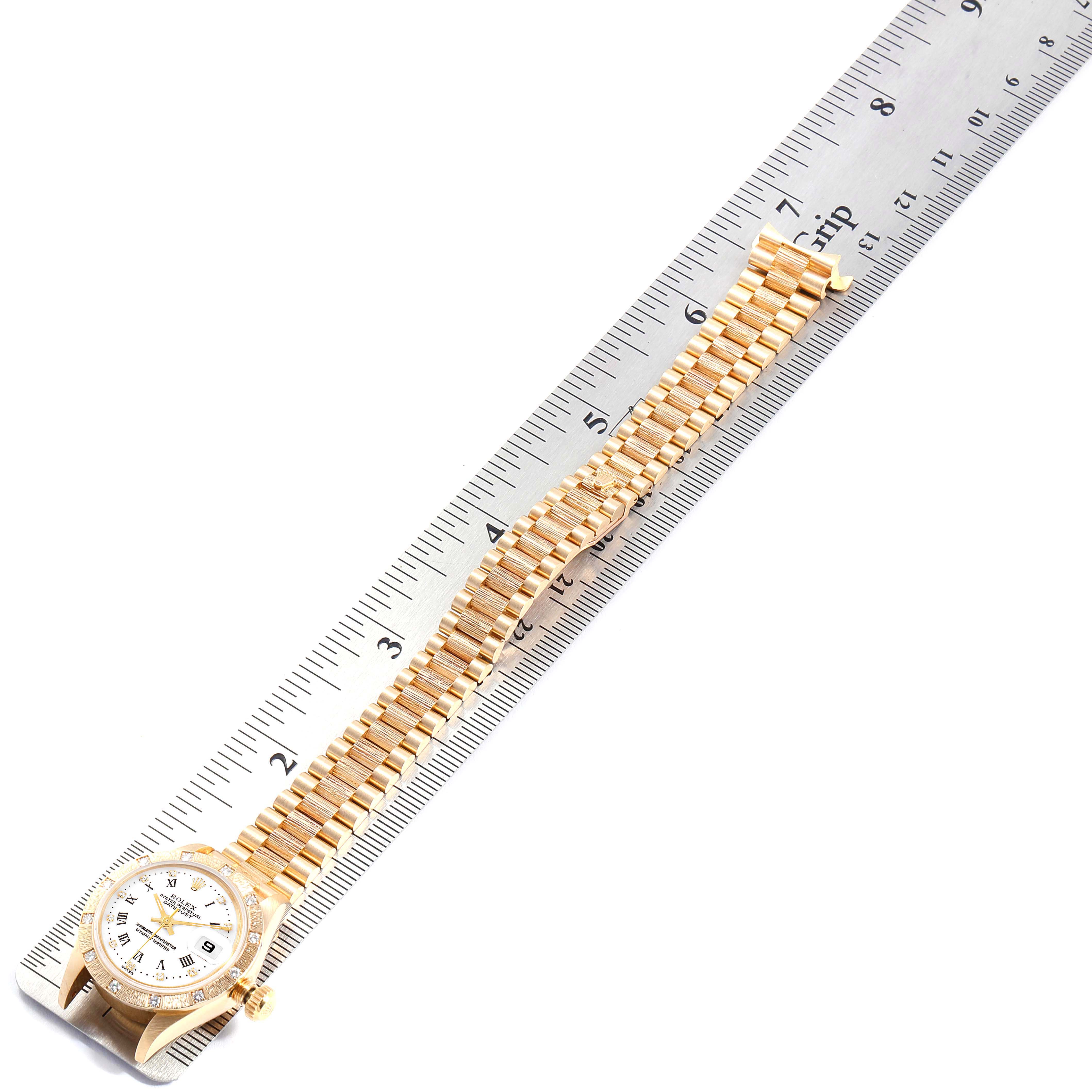 The image shows a Rolex President 69288 Women
s Yellow Gold White Dial 69288 Women
s Yellow Gold White Dial watch laid flat against a ruler, displaying the full length of its band and face from an overhead angle.