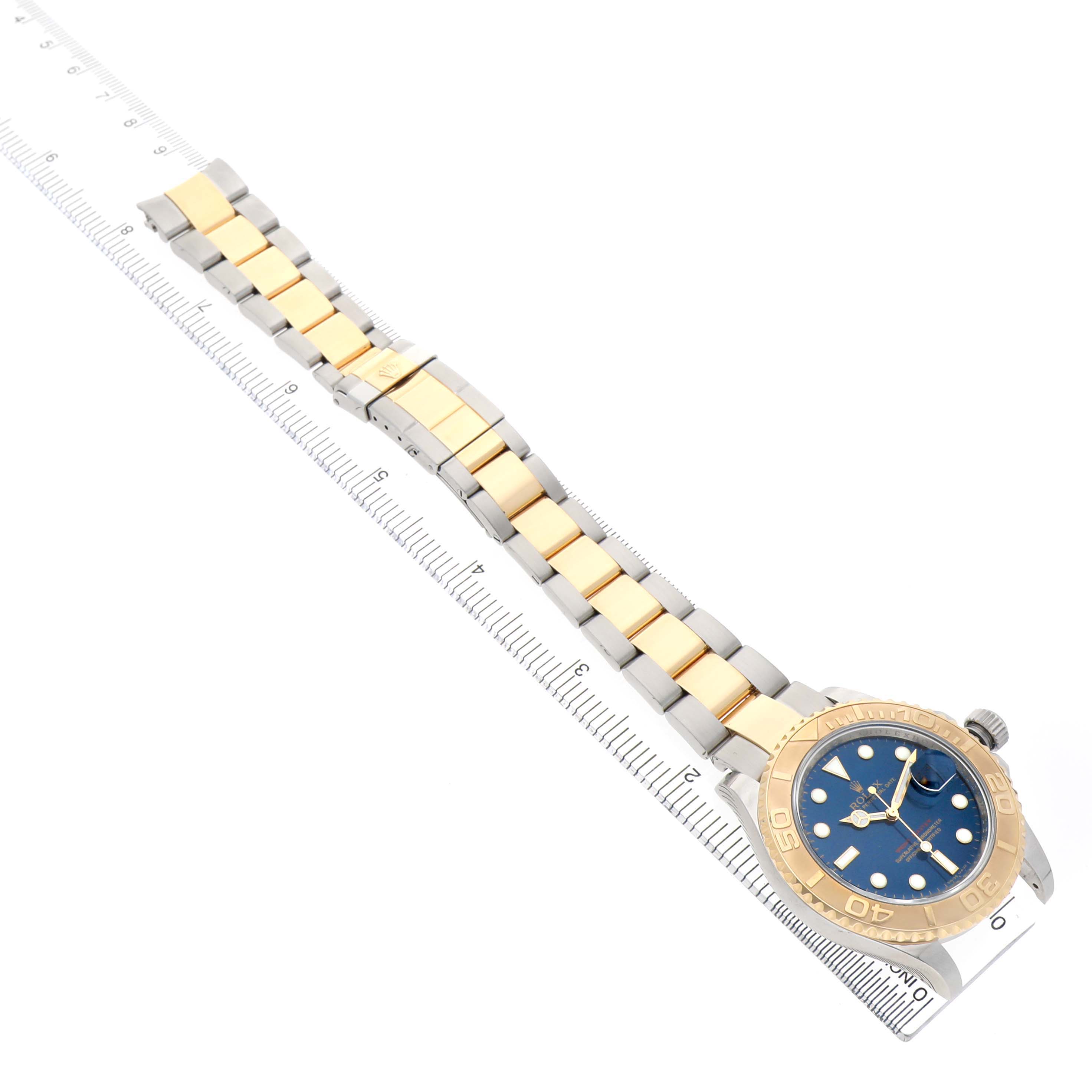 The Rolex Yacht-Master 16623 Men's Steel and Gold (two tone) Blue Dial watch is shown at an angle displaying its face, bezel, bracelet, and clasp with a ruler beside it.