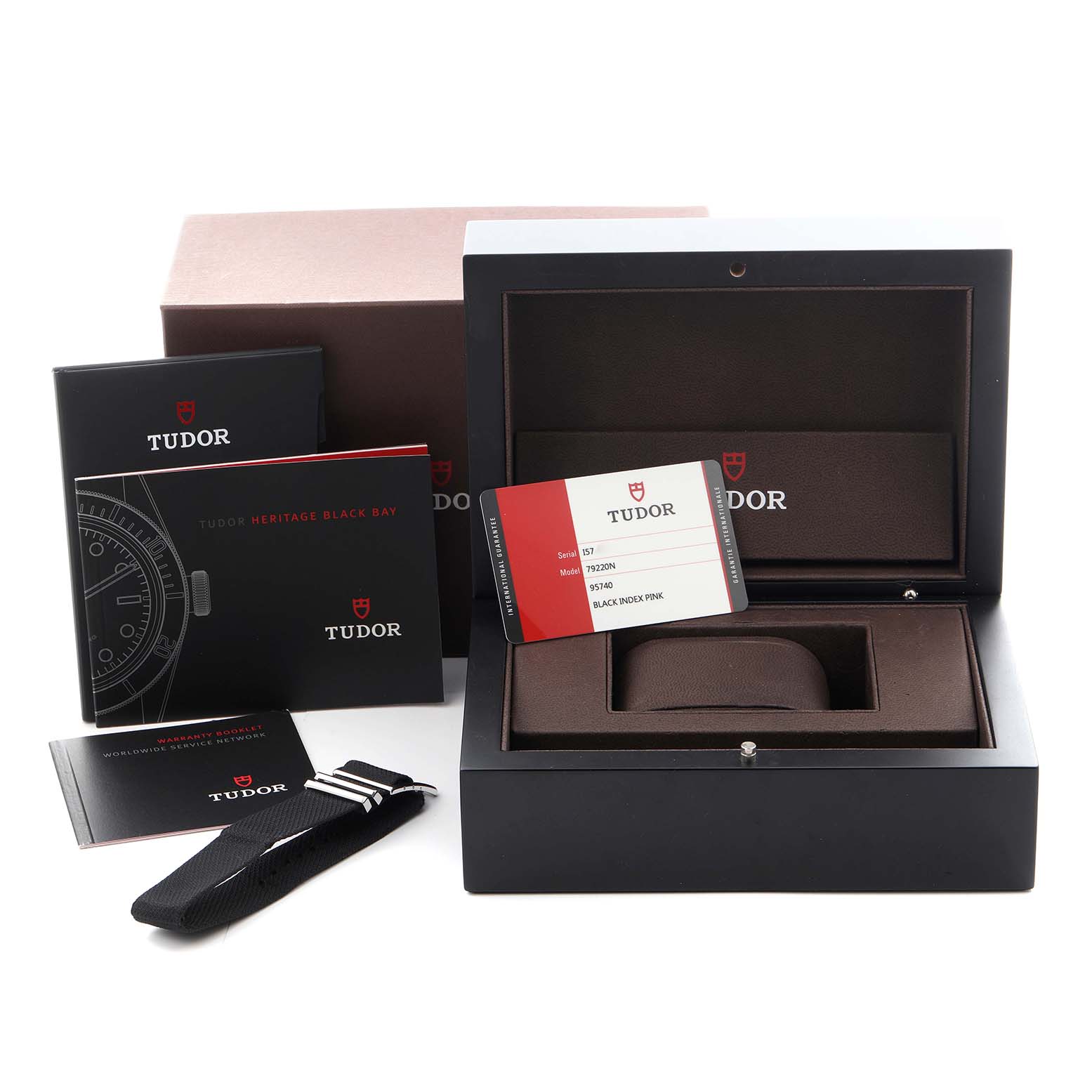 The Tudor Heritage Black Bay 79220N Men's Stainless Steel Black Dial 79220N Men's Stainless Steel Black Dial accessories are shown, including a box, manuals, card, and a fabric strap, all displayed from above.