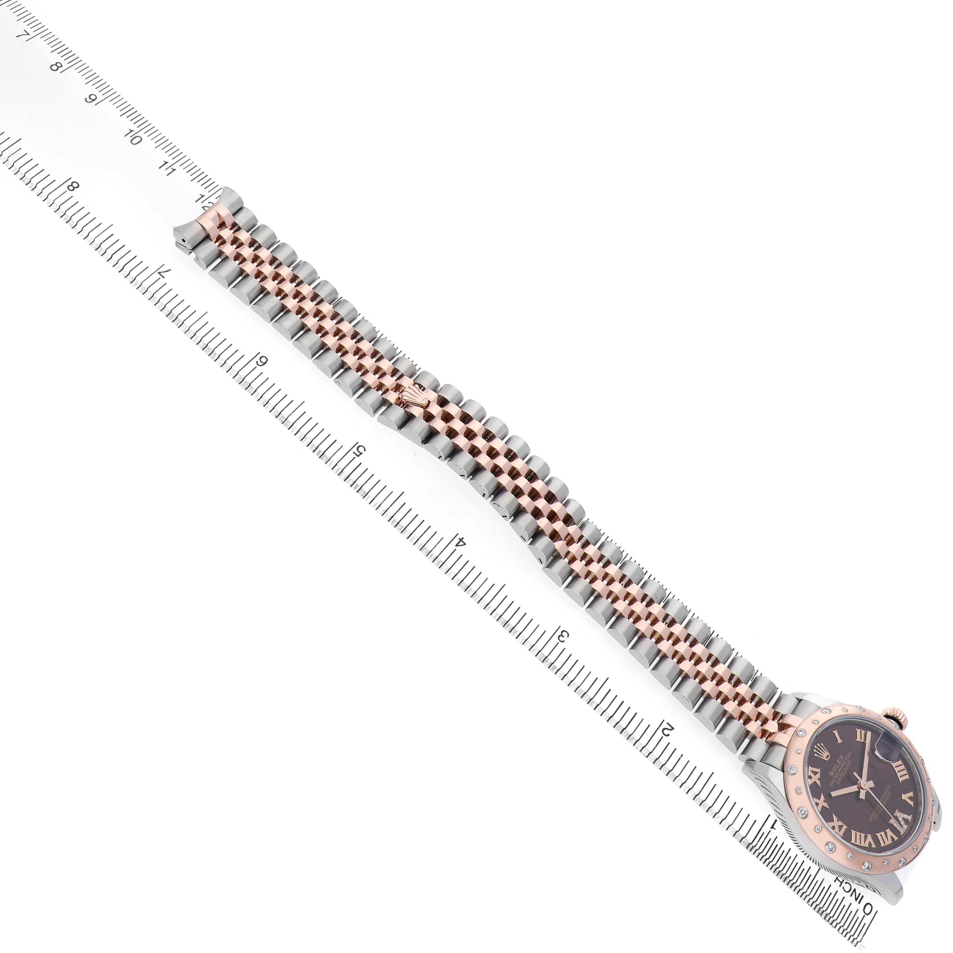 The Rolex Datejust 278341 Women's Steel and Gold (two tone) Brown Dial watch is shown from a top-down angle, highlighting its bracelet and partial face next to a ruler.