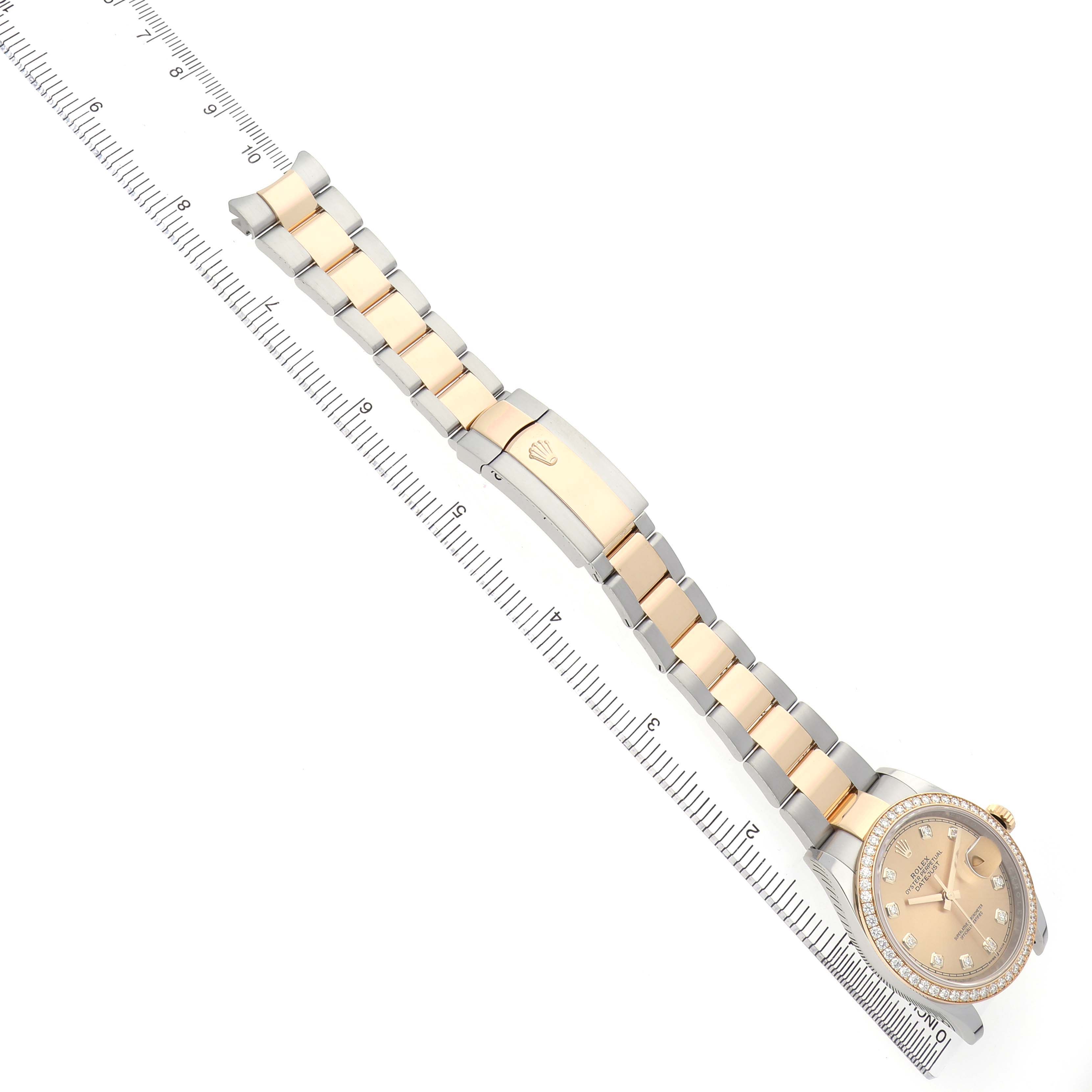 The Rolex Datejust 126283RBR Men's Steel and Gold (two tone) Champagne Dial watch is shown at a diagonal angle, displaying the bracelet, clasp, and face beside a ruler.