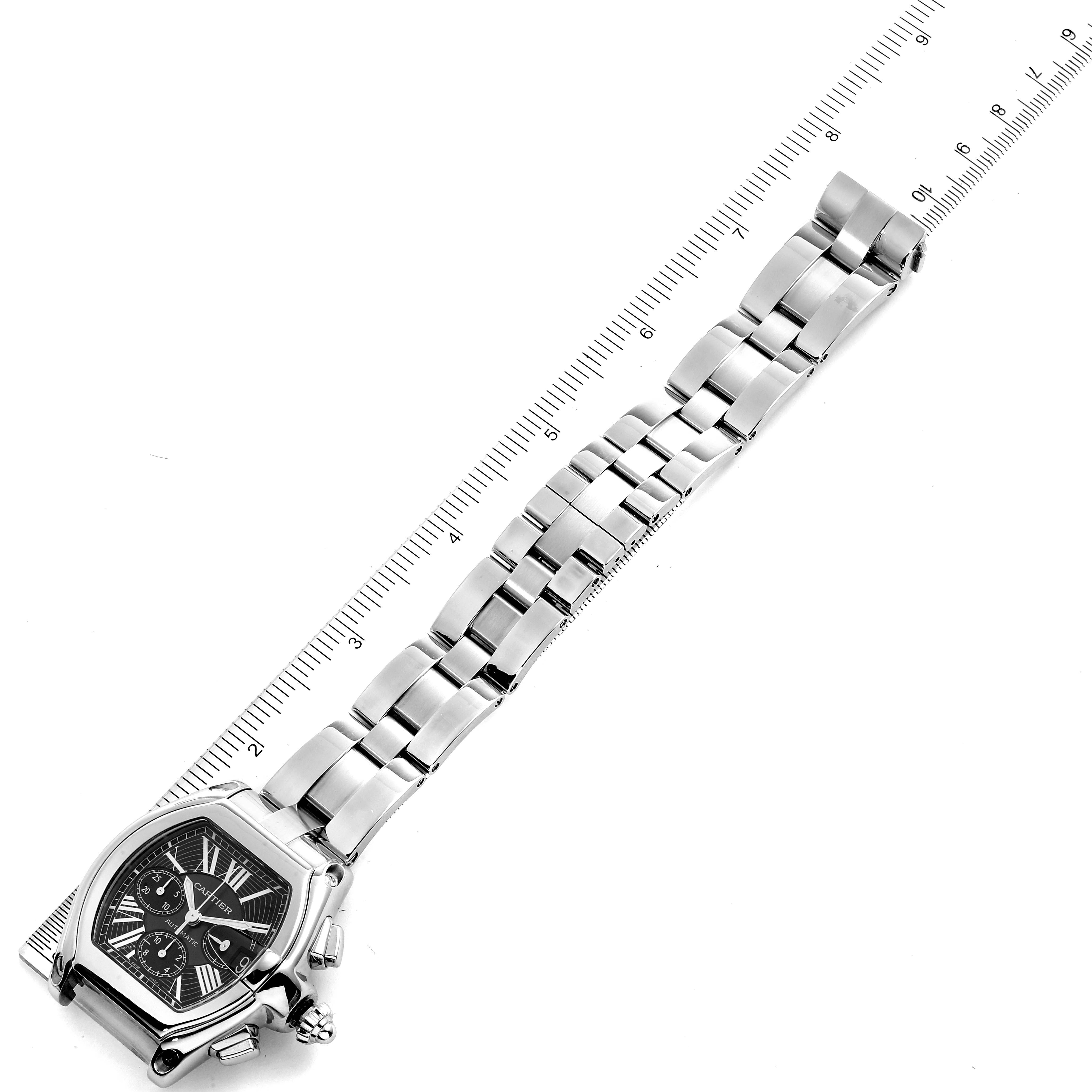 The image shows a Cartier Roadster W62020X6 Men
s Stainless Steel Black Dial W62020X6 Men
s Stainless Steel Black Dial watch with a full view of its face and metal strap alongside a ruler for scale.