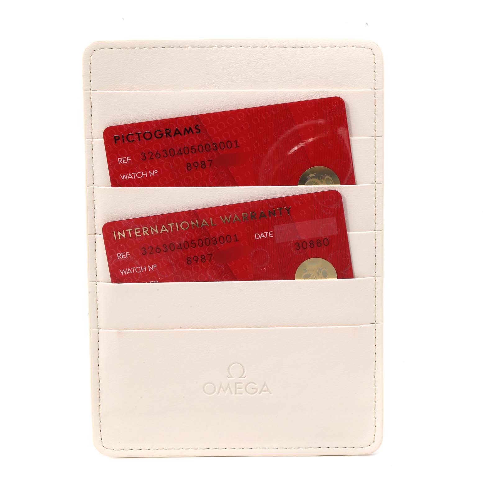 The image shows the warranty and pictograms cards held in a white Omega cardholder for the Speedmaster model.