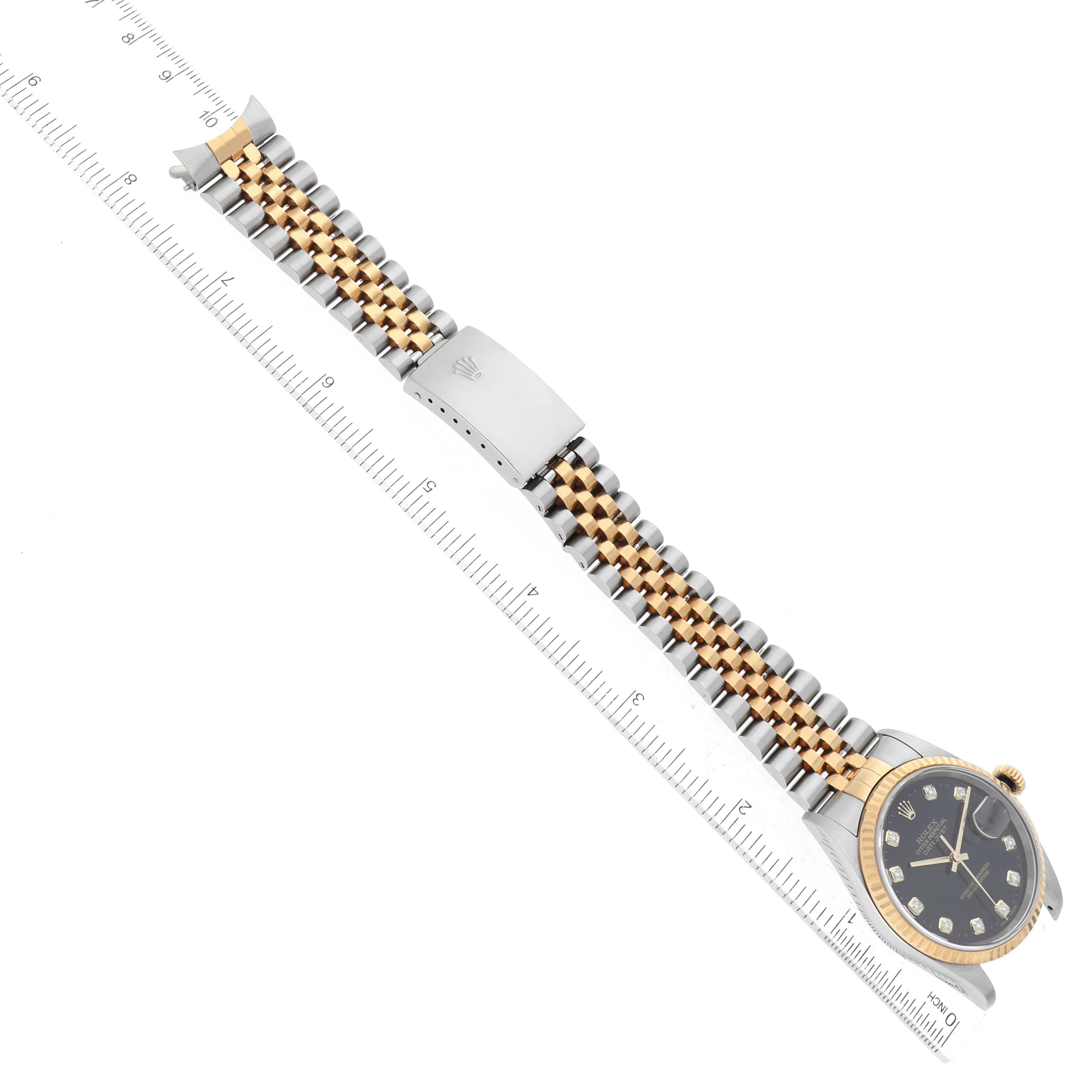 The Rolex Datejust 16233 Men's Steel and Gold (two tone) Black Dial 16233 Men's Steel and Gold (two tone) Black Dial watch is shown from a top-down angle, highlighting its face, bracelet, and clasp positioned next to a ruler.