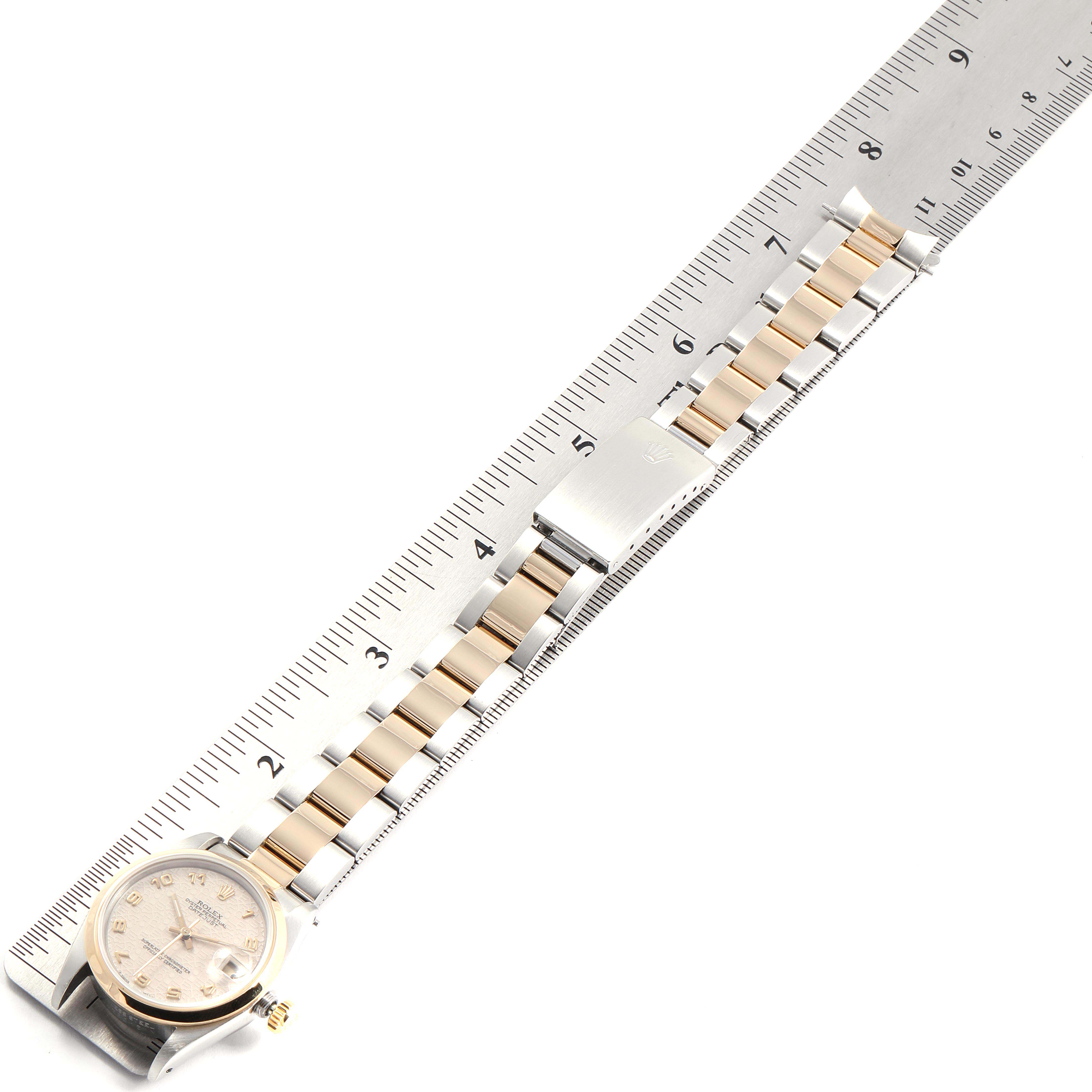 The image shows a top view of a Rolex Mid-Size 68243 Women
s Steel and Gold (two tone) Beige Dial 68243 Women
s Steel and Gold (two tone) Beige Dial model watch, with a focus on the band and clasp, placed alongside a ruler for measurement.