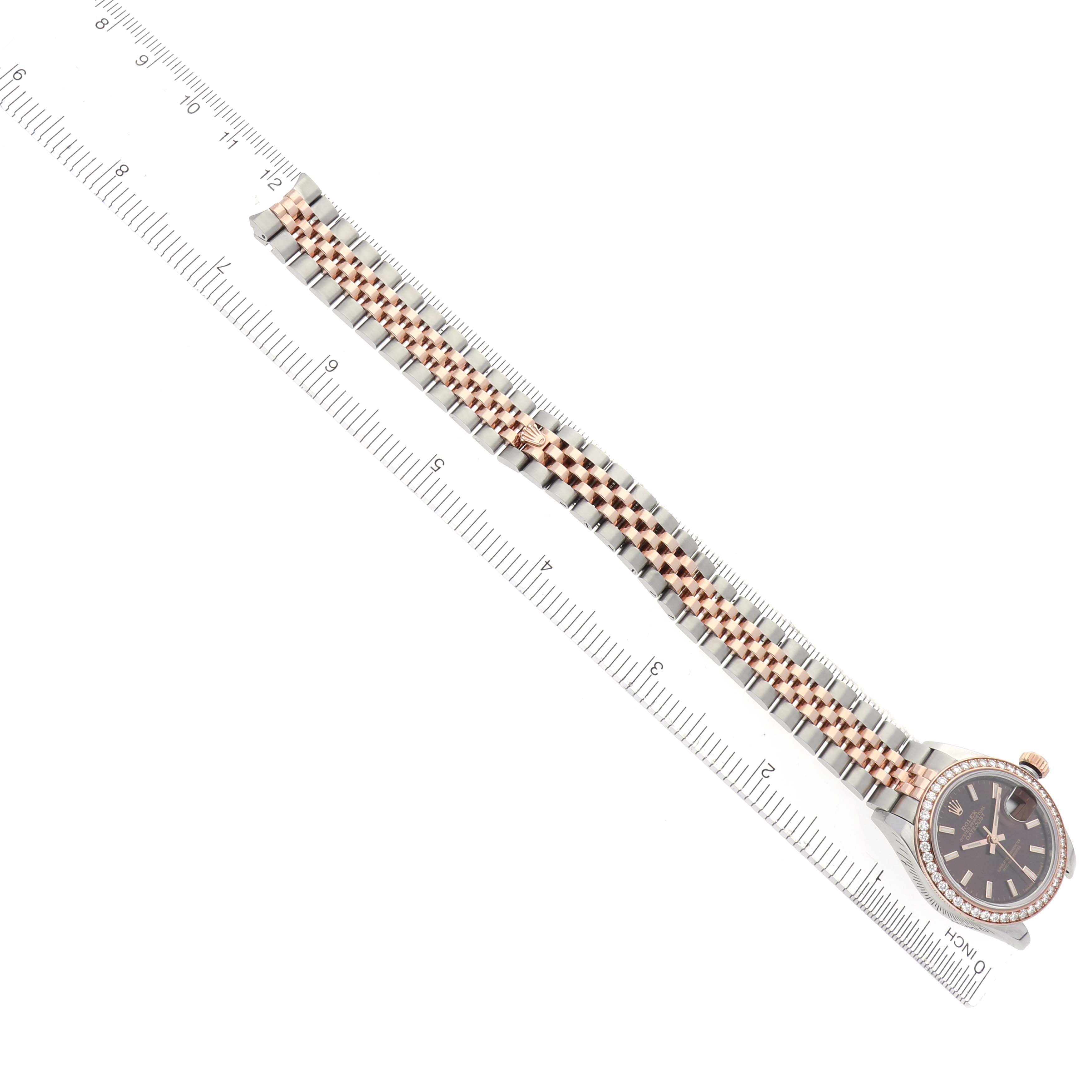 The Rolex Datejust 279381 Women's Steel and Gold (two tone) Brown Dial 279381 Women's Steel and Gold (two tone) Brown Dial watch is shown from an overhead angle, highlighting its band and face beside a ruler for scale.
