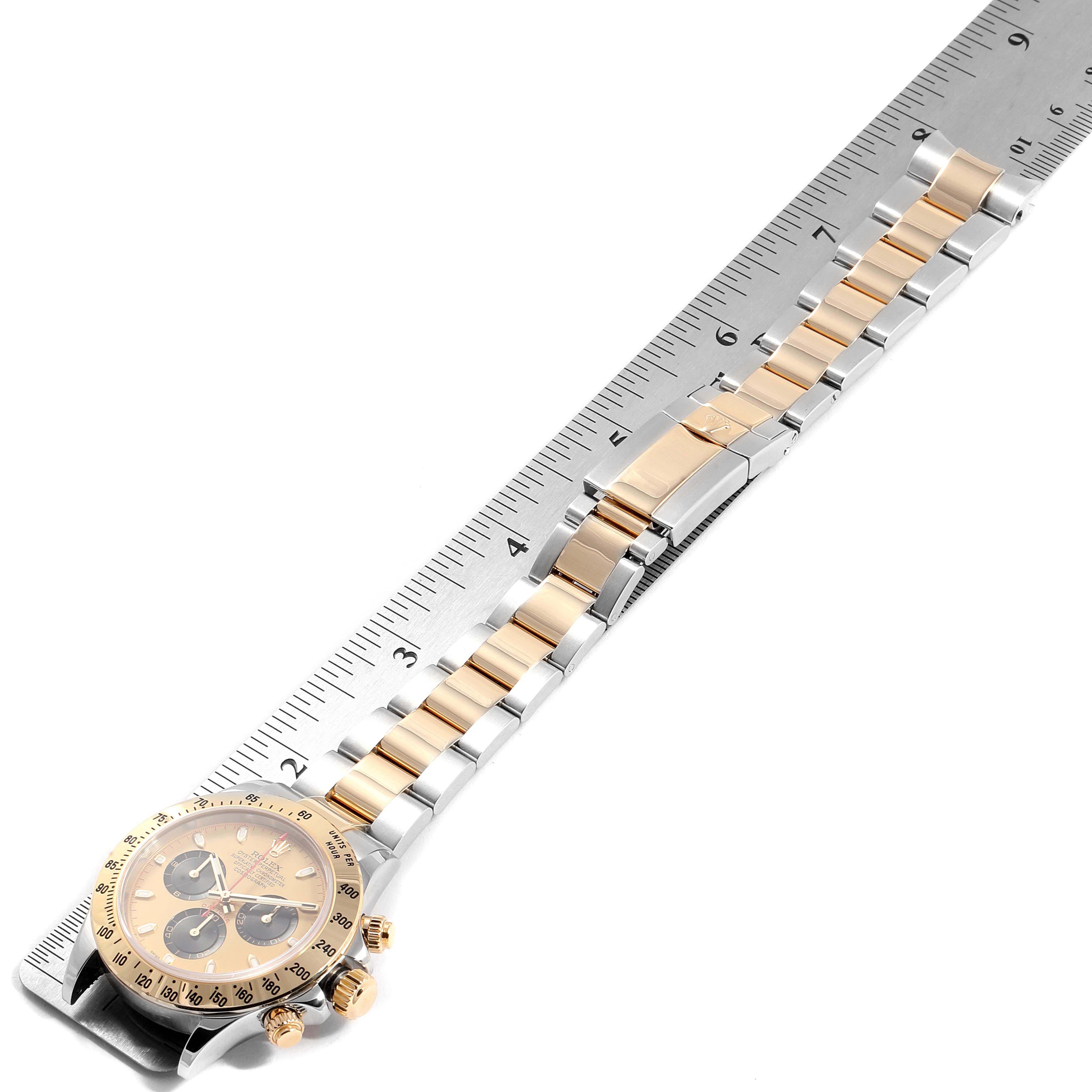 The image shows a Rolex Daytona 116523 Men
s Steel and Gold (two tone) Champagne Dial 116523 Men
s Steel and Gold (two tone) Champagne Dial watch lying flat next to a ruler, highlighting its bracelet and bezel from a top-down angle.