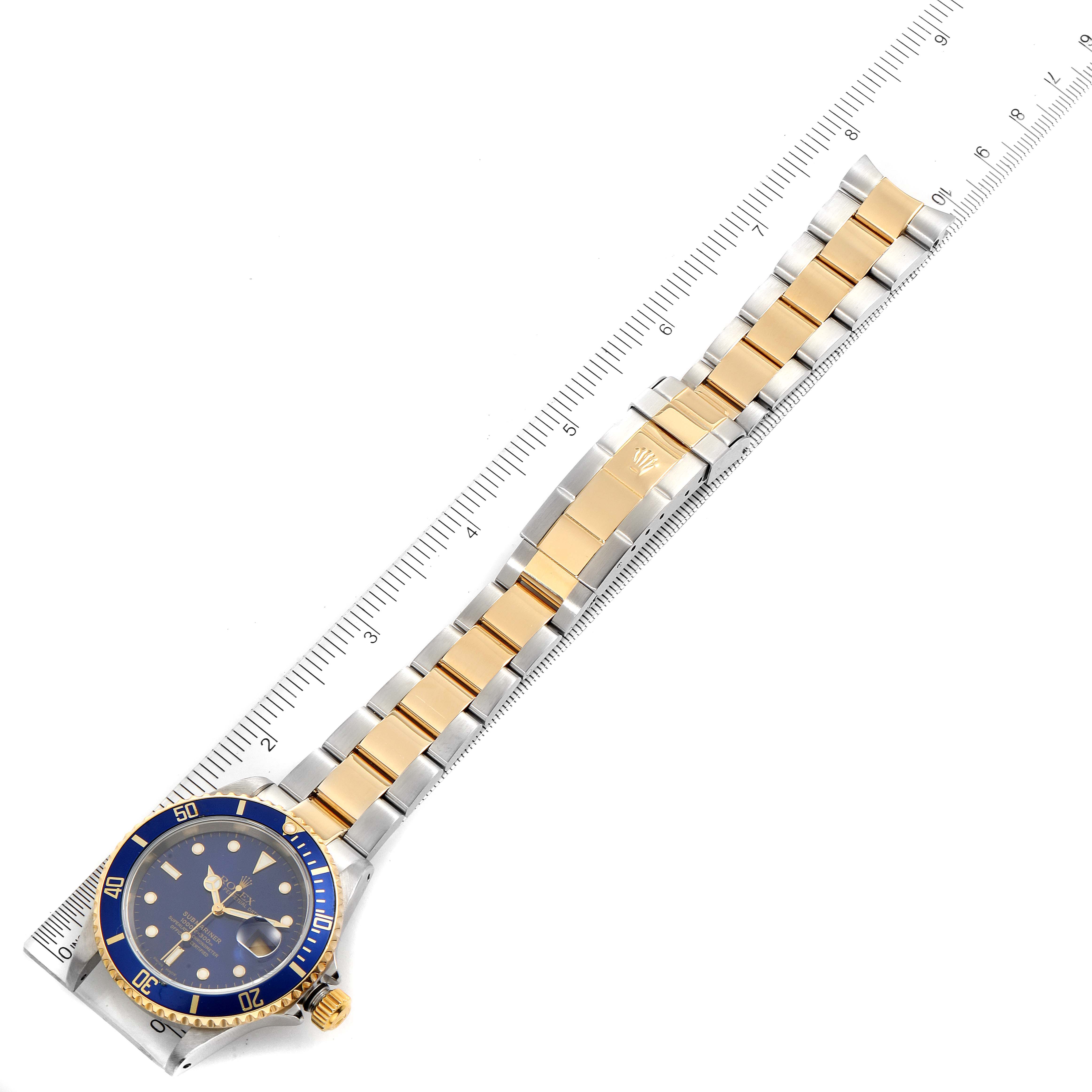This Rolex Submariner 16613 Men
s Steel and Gold (two tone) Blue Dial 16613 Men
s Steel and Gold (two tone) Blue Dial watch is shown from a top-down angle, displaying its face, bezel, and bracelet, with a ruler for scale.
