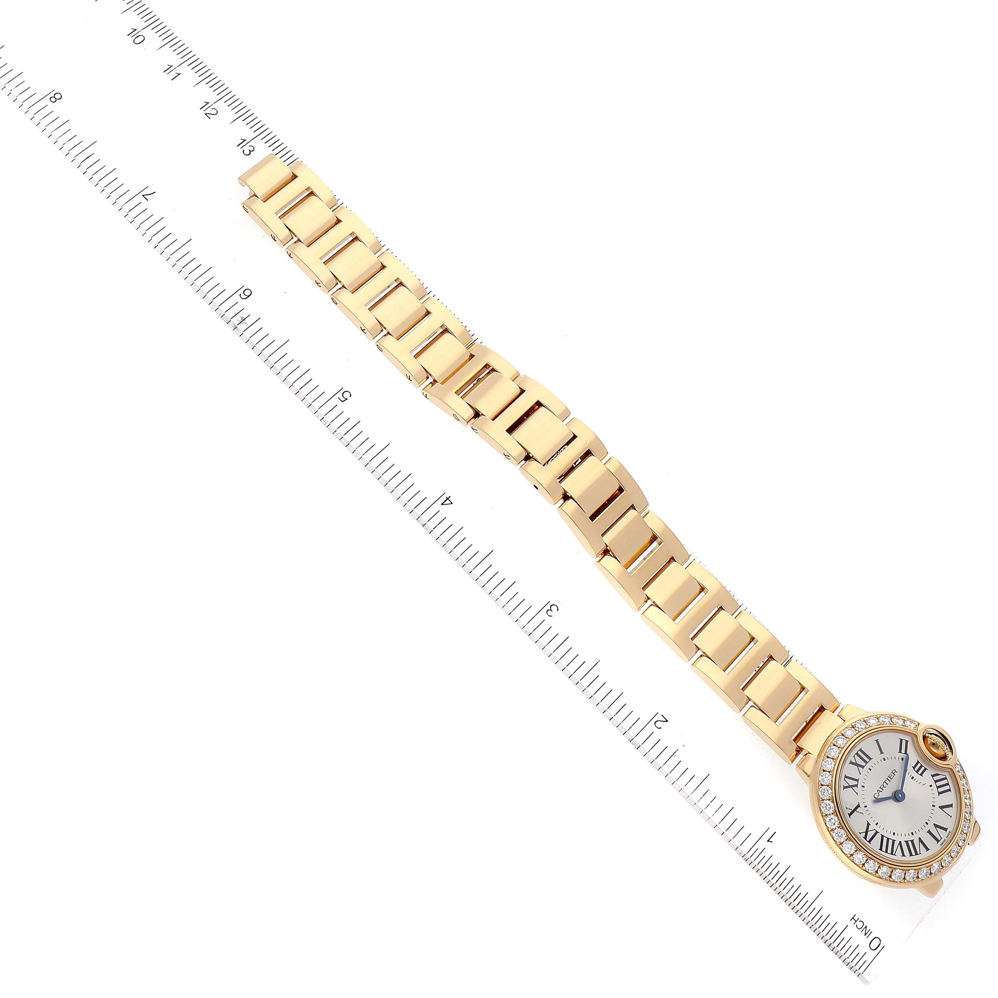The image shows an overhead view of a Cartier Ballon Bleu WE9001Z3 Women's Yellow Gold Silver Dial WE9001Z3 Women's Yellow Gold Silver Dial watch with a gold bracelet next to a ruler.