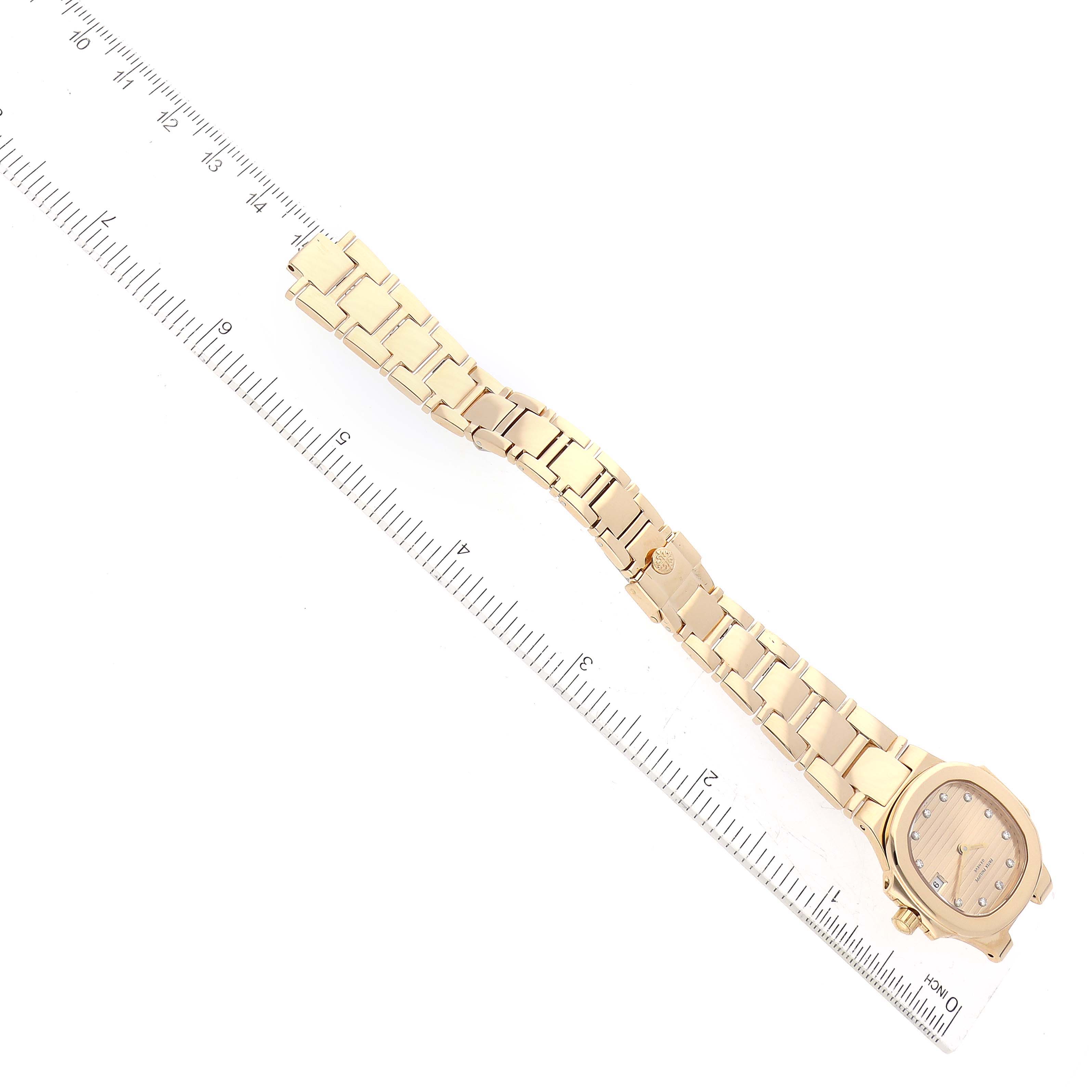 This image shows the Patek Philippe Nautilus 4700/51 Women's Yellow Gold Champagne Dial 4700/51 Women's Yellow Gold Champagne Dial watch angled diagonally, displaying the face, bracelet, and a ruler measurement for scale.