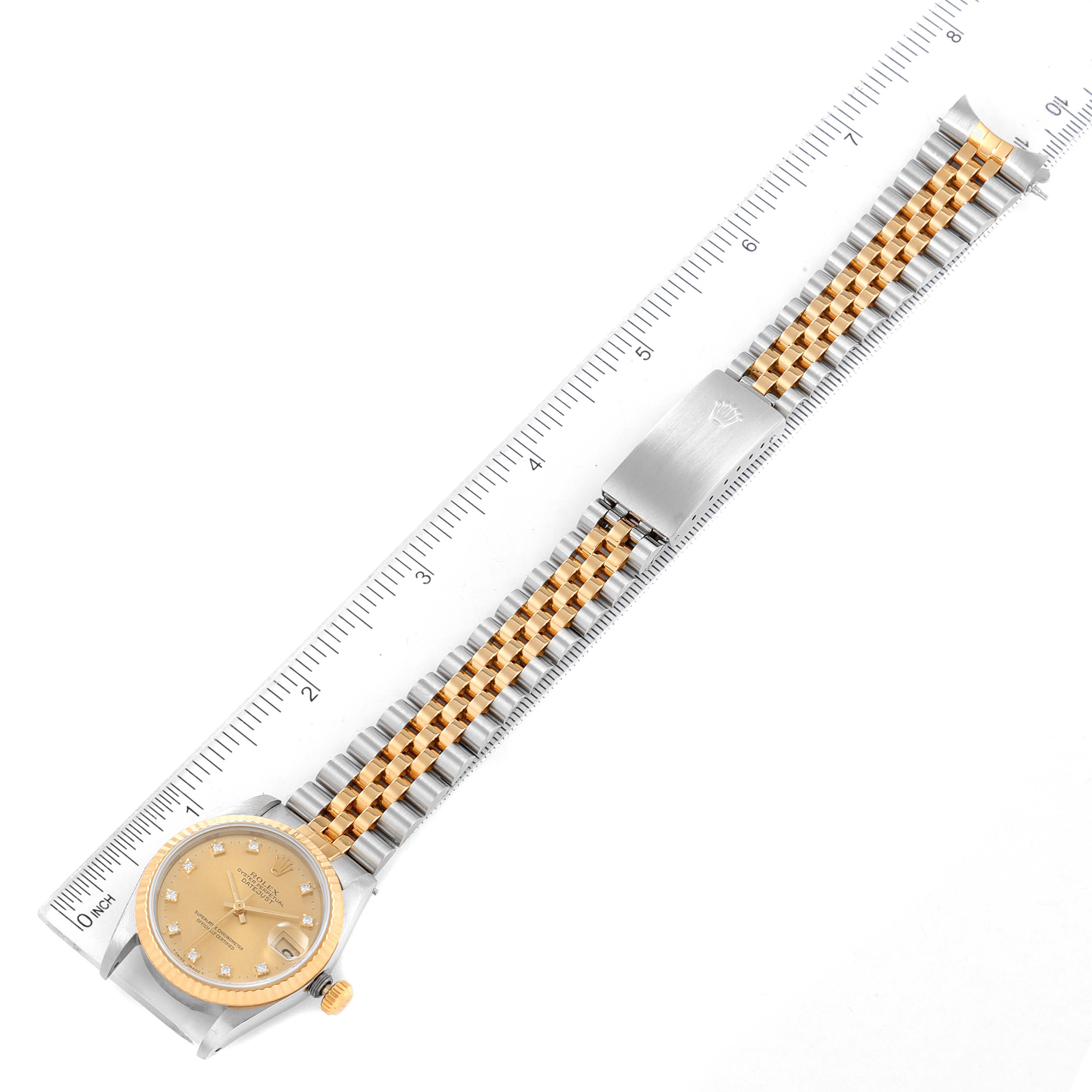 The image shows the top view of a Rolex Mid-Size 68273 Women
s Steel and Gold (two tone) Champagne Dial 68273 Women
s Steel and Gold (two tone) Champagne Dial watch with a gold dial, two-tone bracelet, and a ruler for scale.