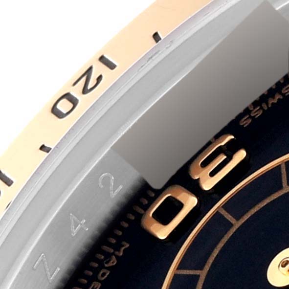 This close-up image of the Rolex Daytona 116523 Men
s Steel and Gold (two tone) Black Dial 116523 Men
s Steel and Gold (two tone) Black Dial watch shows a portion of the bezel with numeric engravings and a part of the dial.