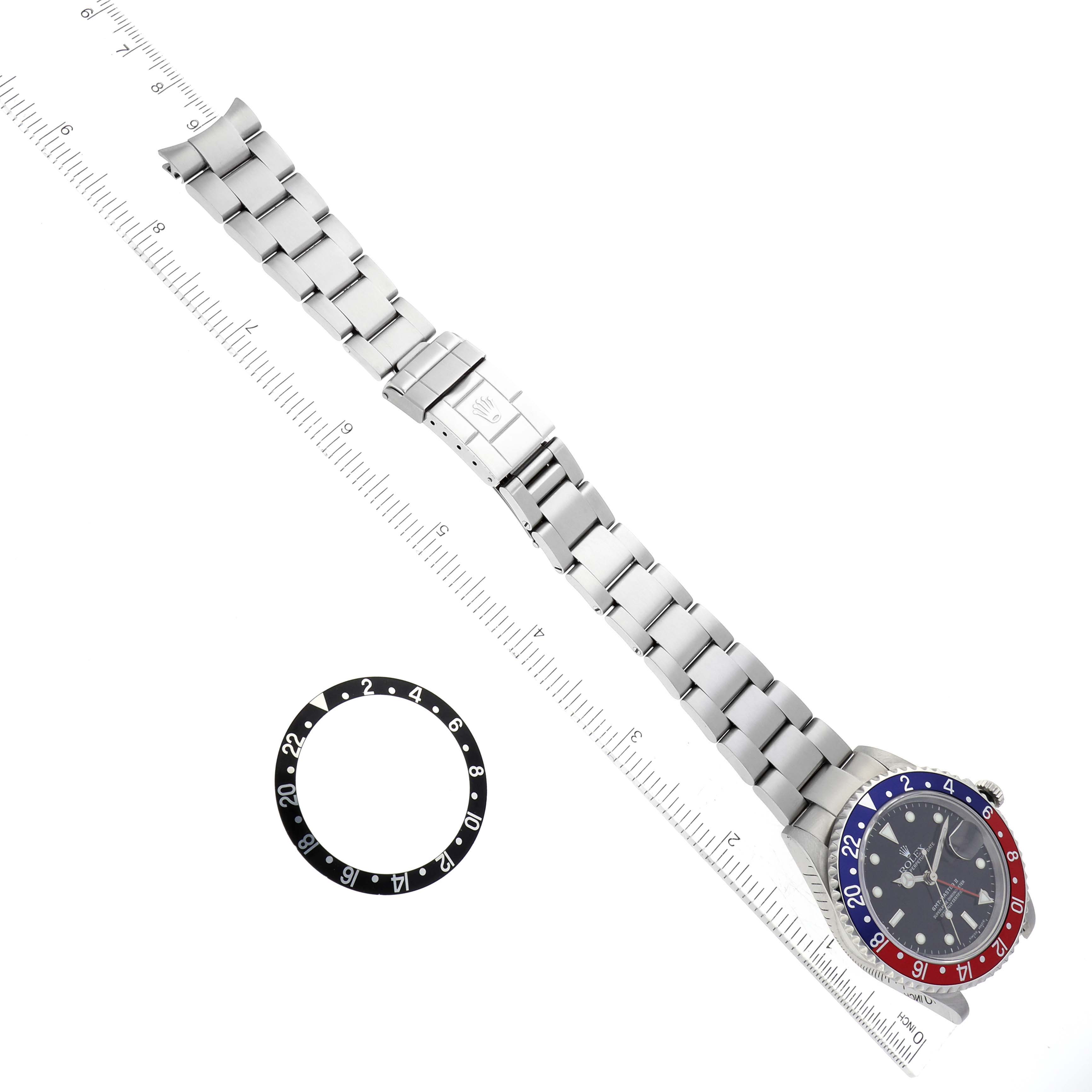 This image shows a top-down view of a Rolex GMT-Master 16710 Men's Stainless Steel Black Dial 16710 Men's Stainless Steel Black Dial watch, its bezel ring, and a ruler for scale.