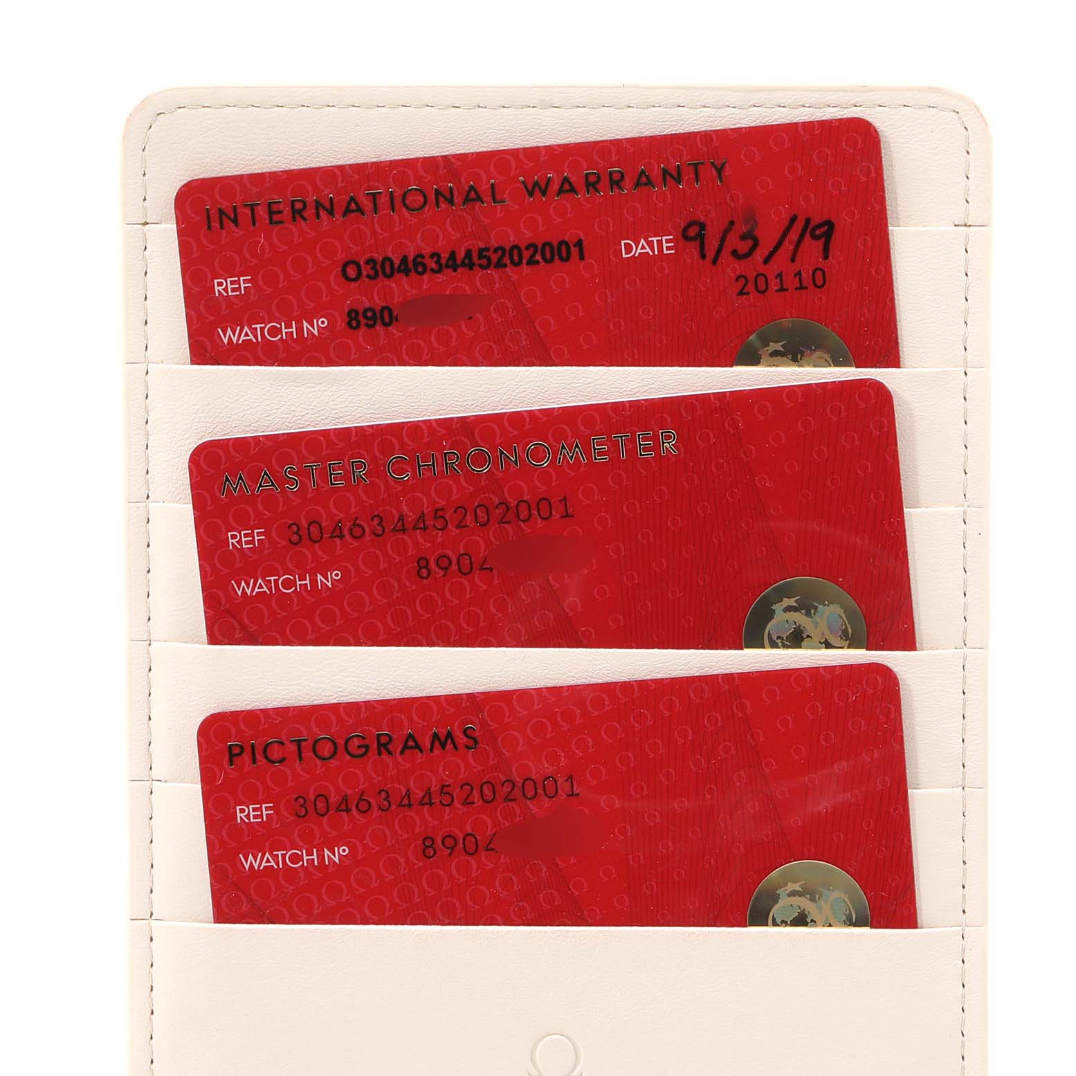 The image shows three warranty and certification cards for an Omega Speedmaster 304.63.44.52.02.001  Men's Yellow Gold Silver Dial 304.63.44.52.02.001  Men's Yellow Gold Silver Dial watch in a holder, viewed from the front.