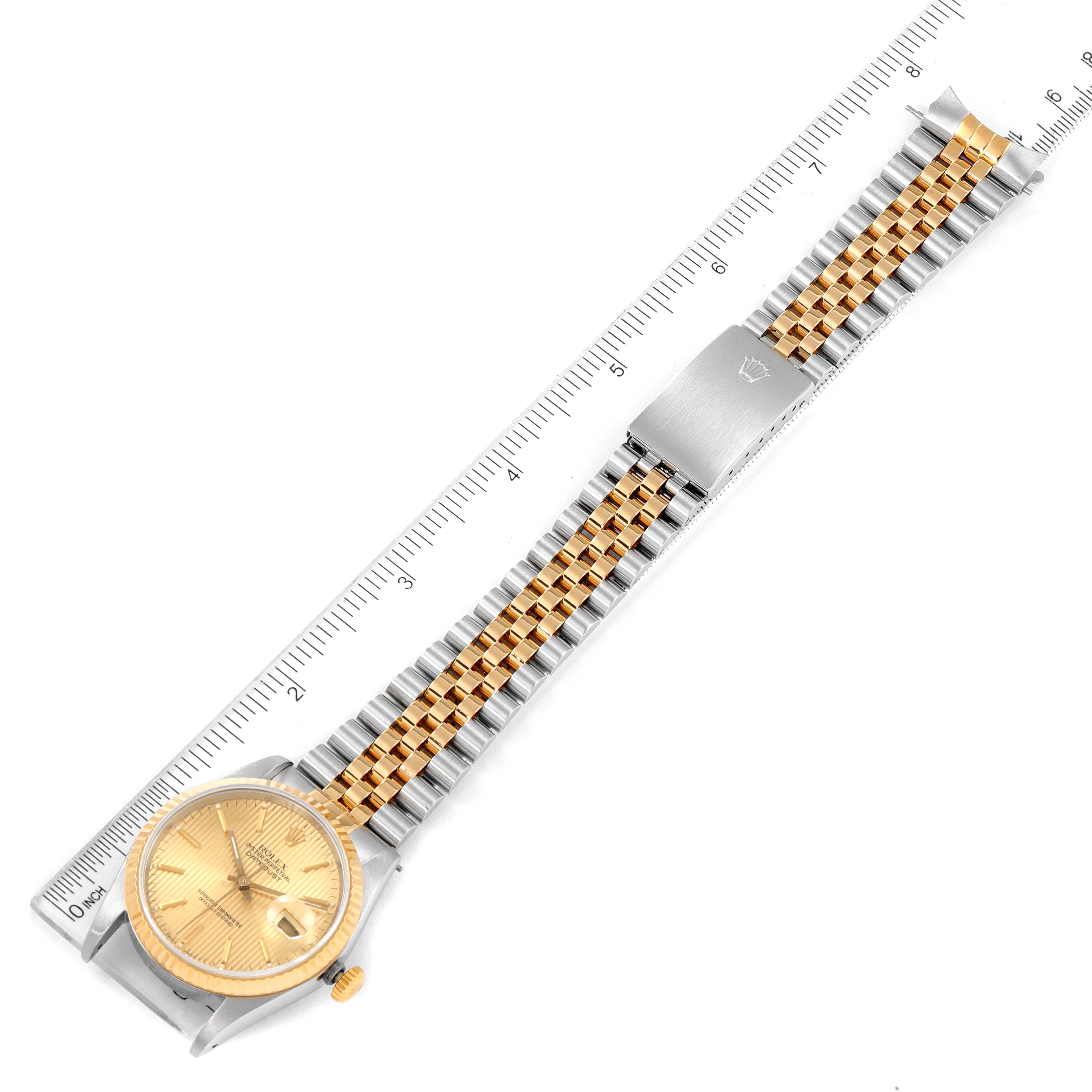 The image shows a Rolex Datejust 16233 Men
s Steel and Gold (two tone) Champagne Dial 16233 Men
s Steel and Gold (two tone) Champagne Dial watch, with a gold and stainless steel bracelet, positioned diagonally alongside a ruler.
