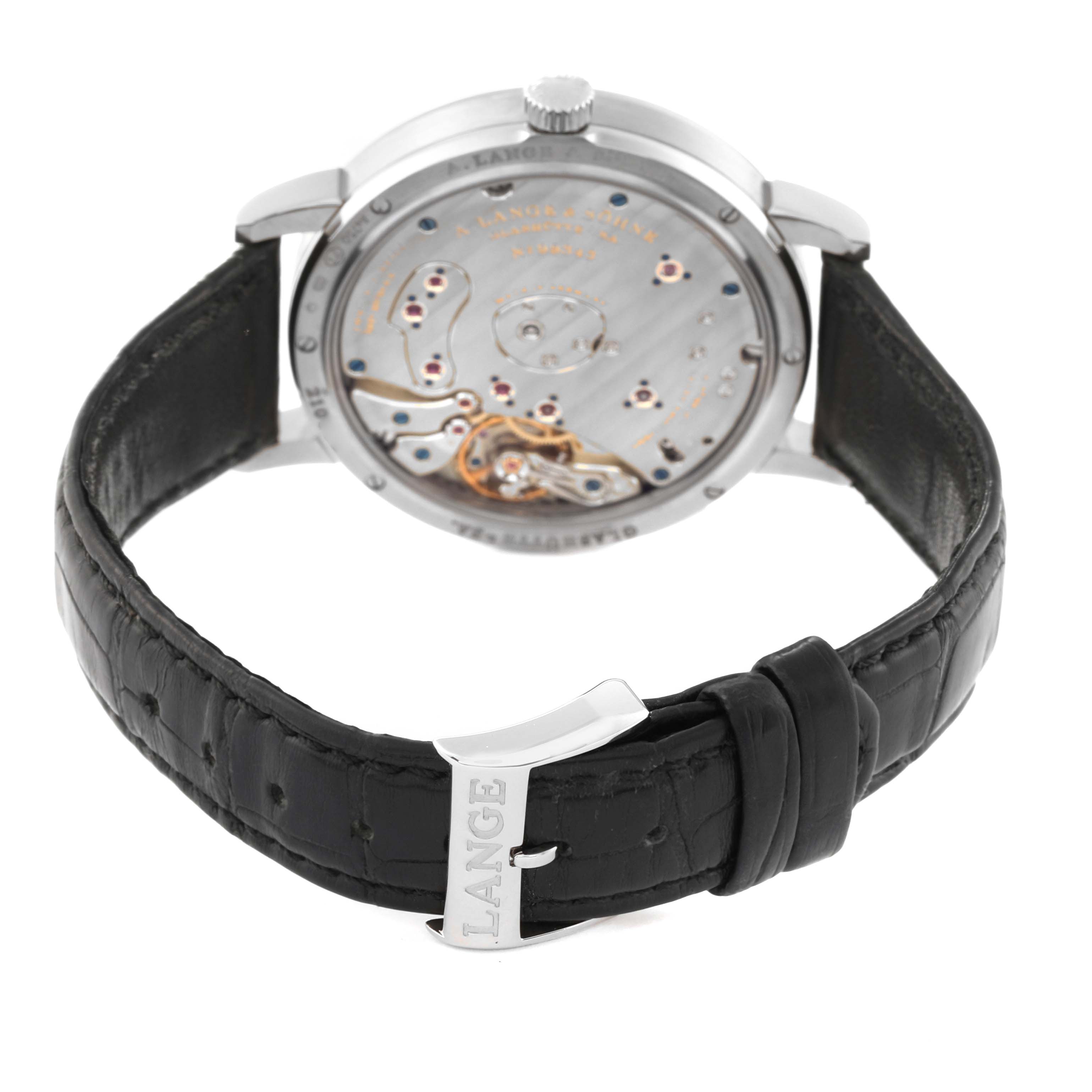 The image shows the back view of the A. Lange & Sohne Lange 1 117.028 Men's White Gold Black Dial watch, highlighting its mechanical movement and leather strap with a Lange buckle.